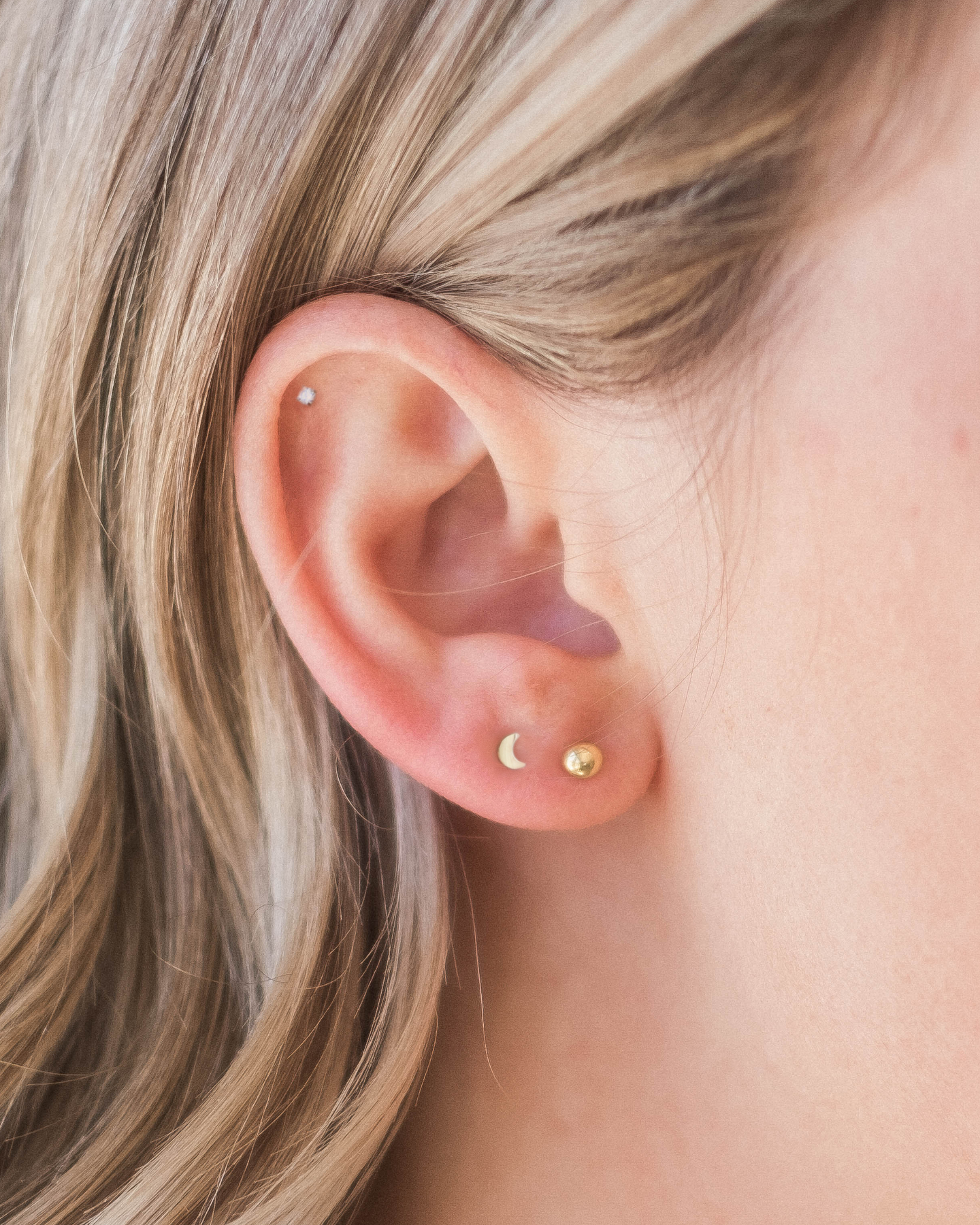 A close-up view of a person's ear with two small earrings, one with a moon symbol and the other with a crescent moon symbol.