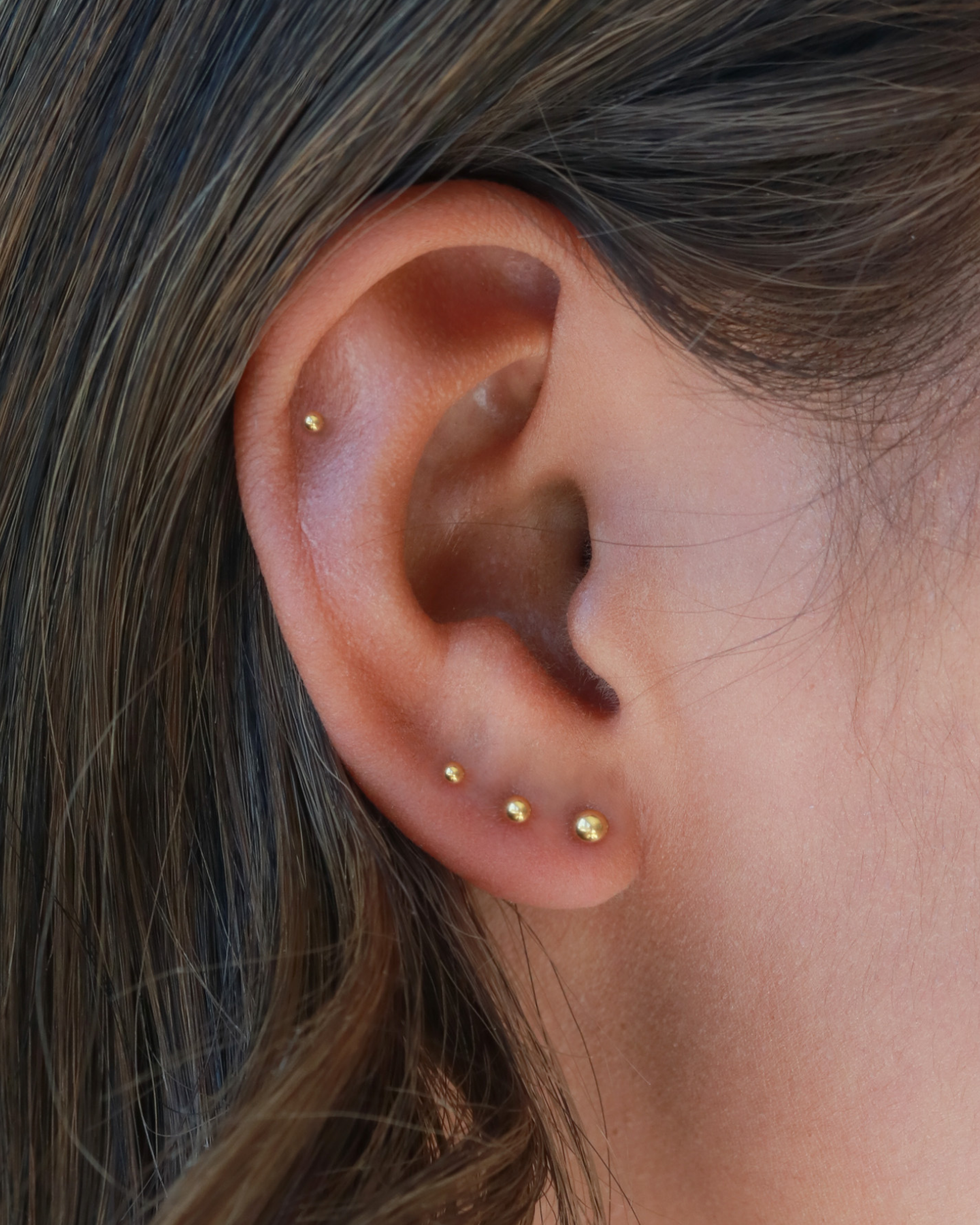 A close-up view of a person's ear adorned with multiple gold earrings.