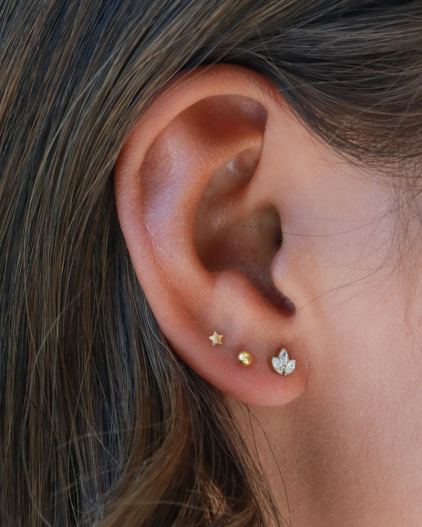 A close-up view of a person's ear adorned with three small gold earrings, each featuring a different design.