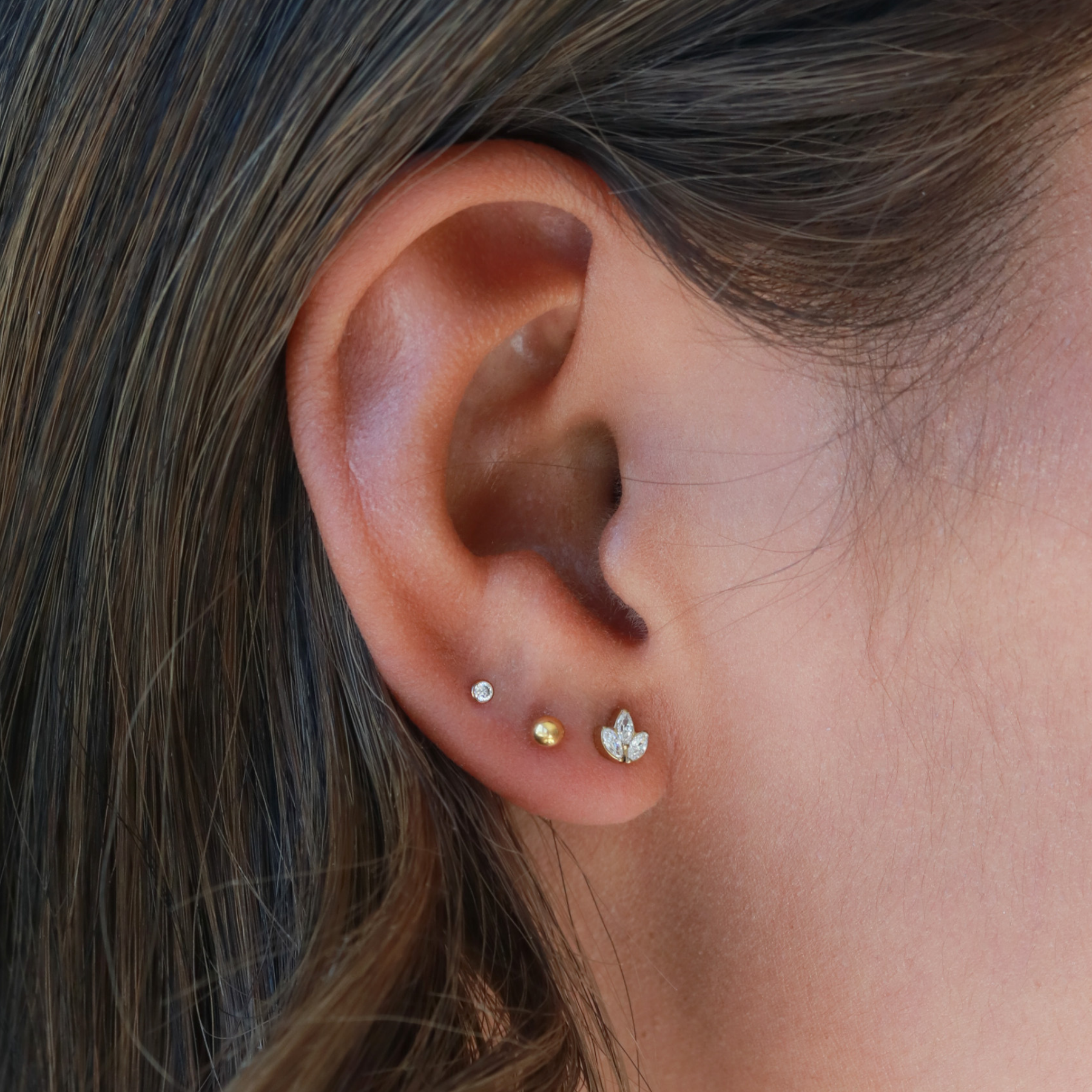 A close-up view of a person's ear adorned with multiple earrings, including three small gold earrings and one larger gold earring.
