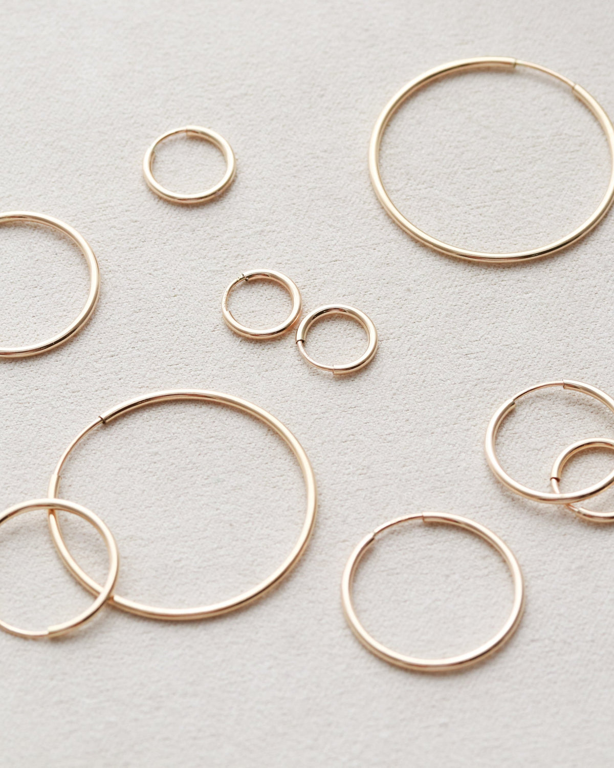 Gold hoop earrings of various sizes on a light gray background