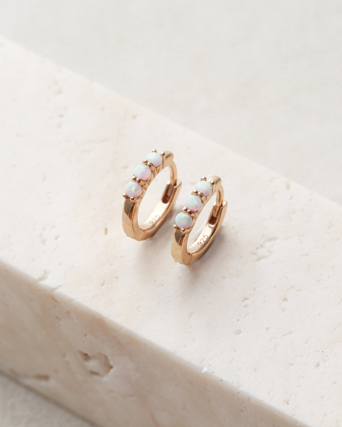 Rose gold hoop earrings with small stones on a beige stone surface