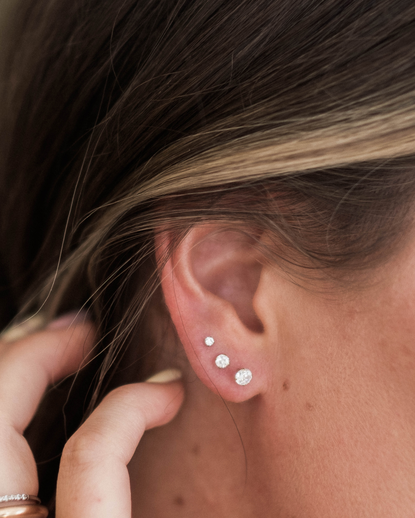 A close-up view of a person's ear adorned with three small, round, white earrings.