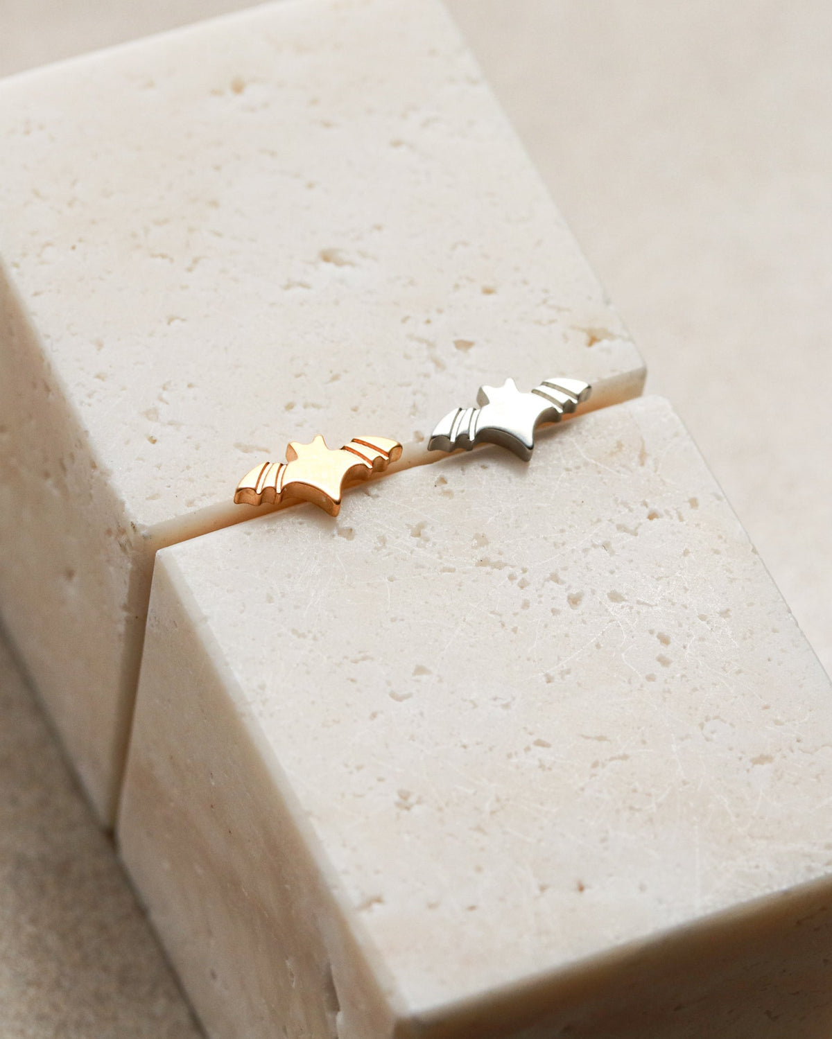 Two small star-shaped earrings are placed on a white rectangular block.