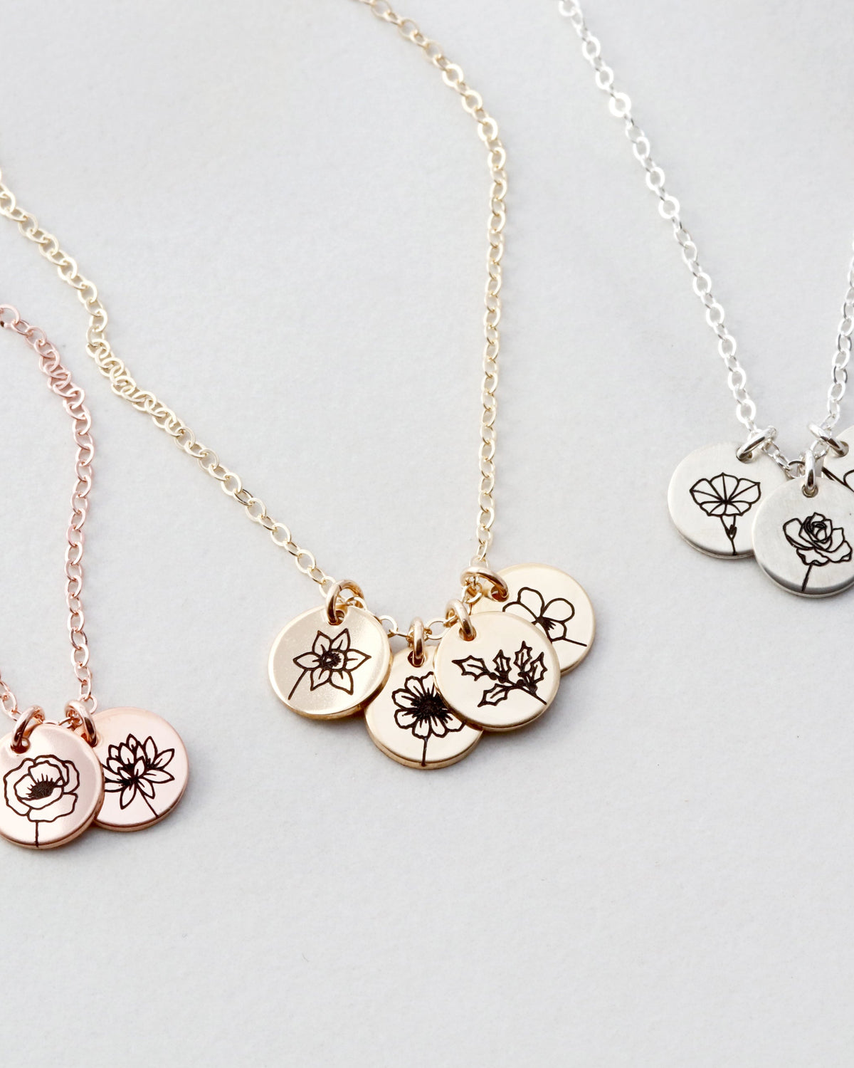 Three necklaces with floral engraved pendants on a light gray background