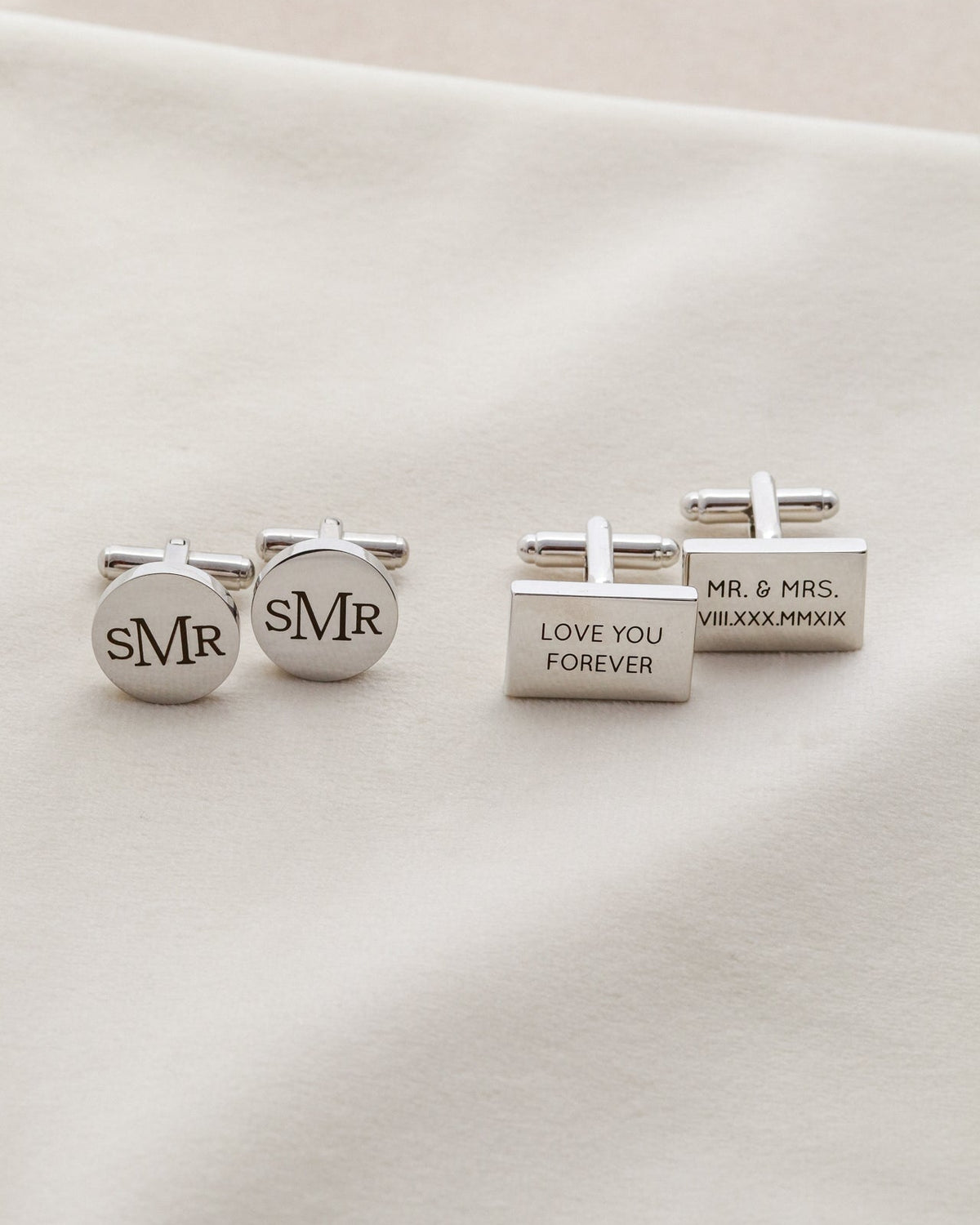 Three silver cufflinks with engraved text on a white surface
