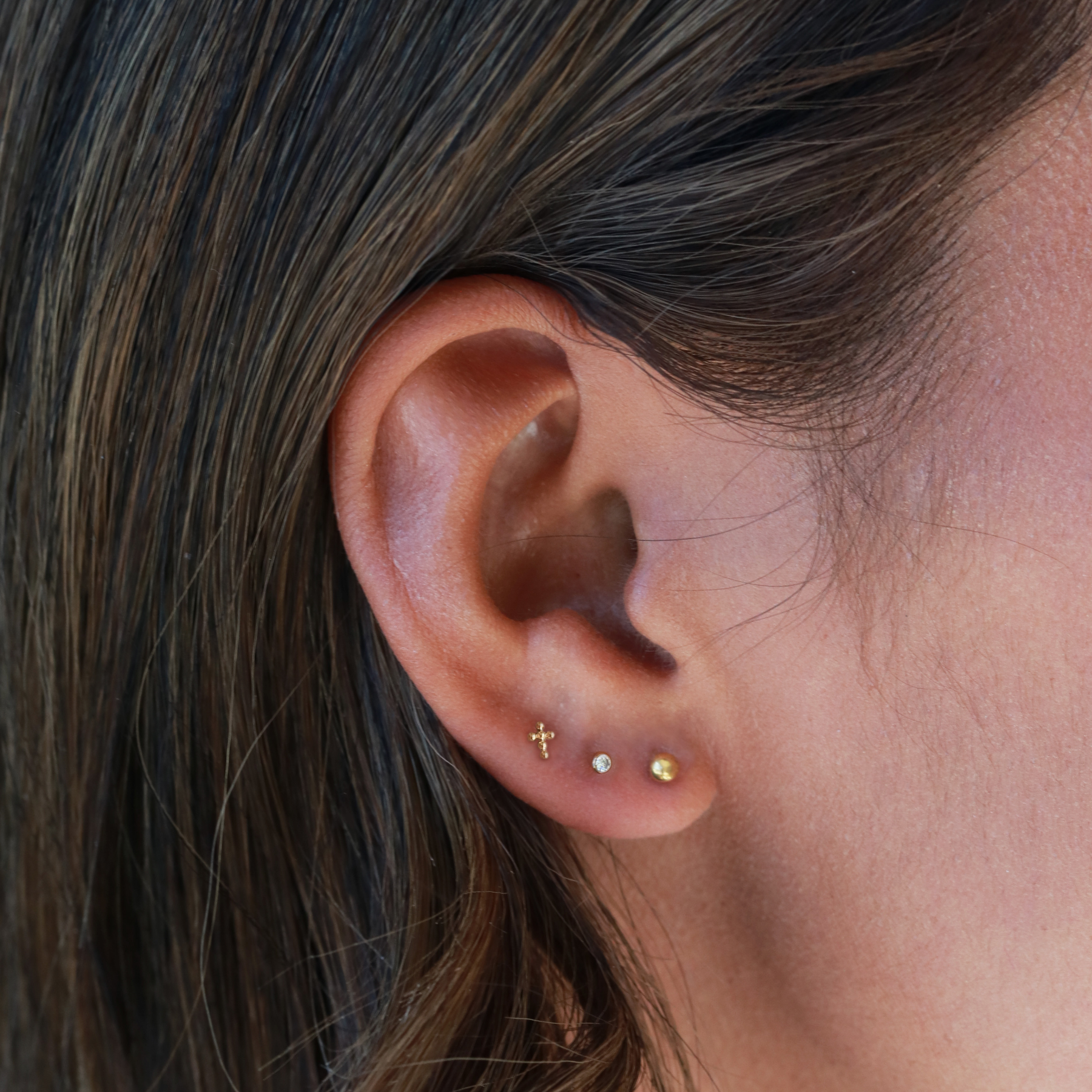 A close-up view of a person's ear adorned with three small gold earrings.