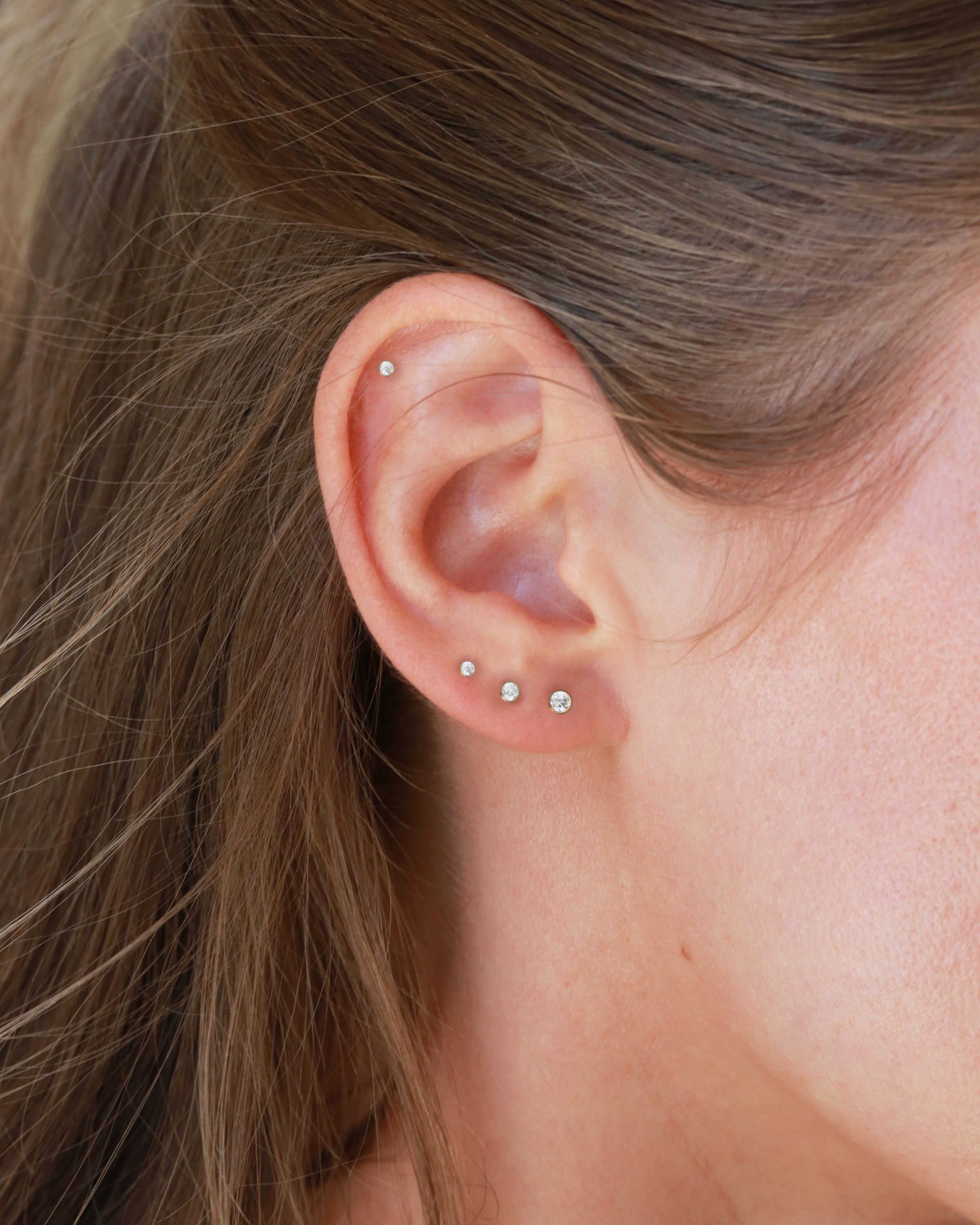 a close-up view of a person's ear adorned with multiple small earrings.