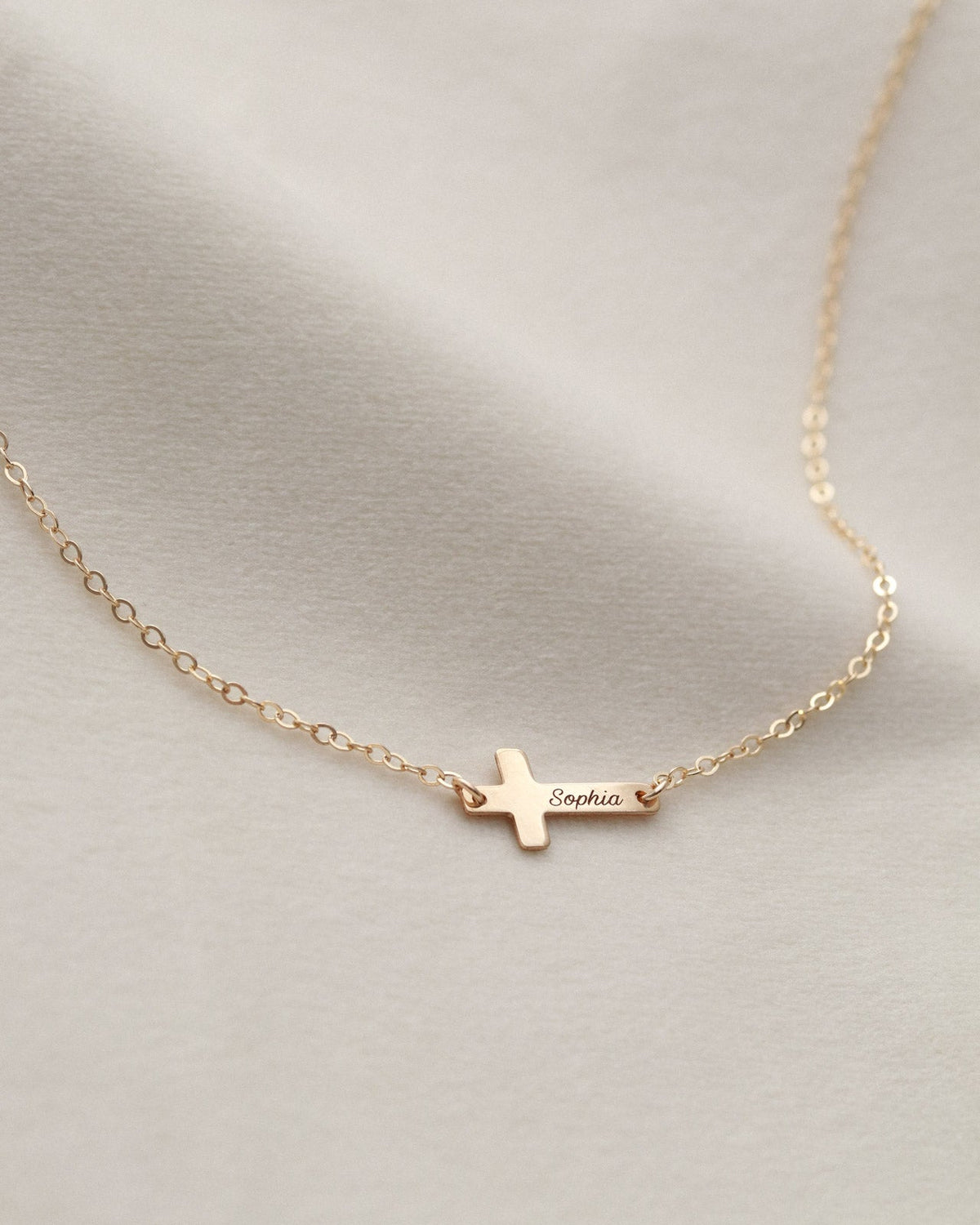 Gold necklace with a small cross pendant on a light gray background