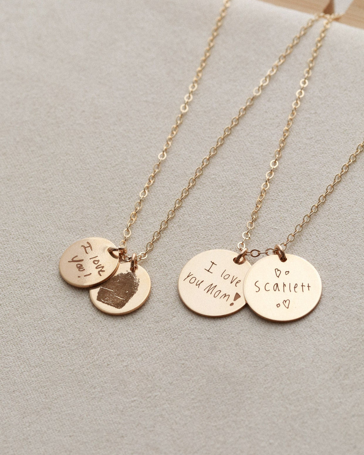 Two gold necklaces with engraved pendants on a light gray surface