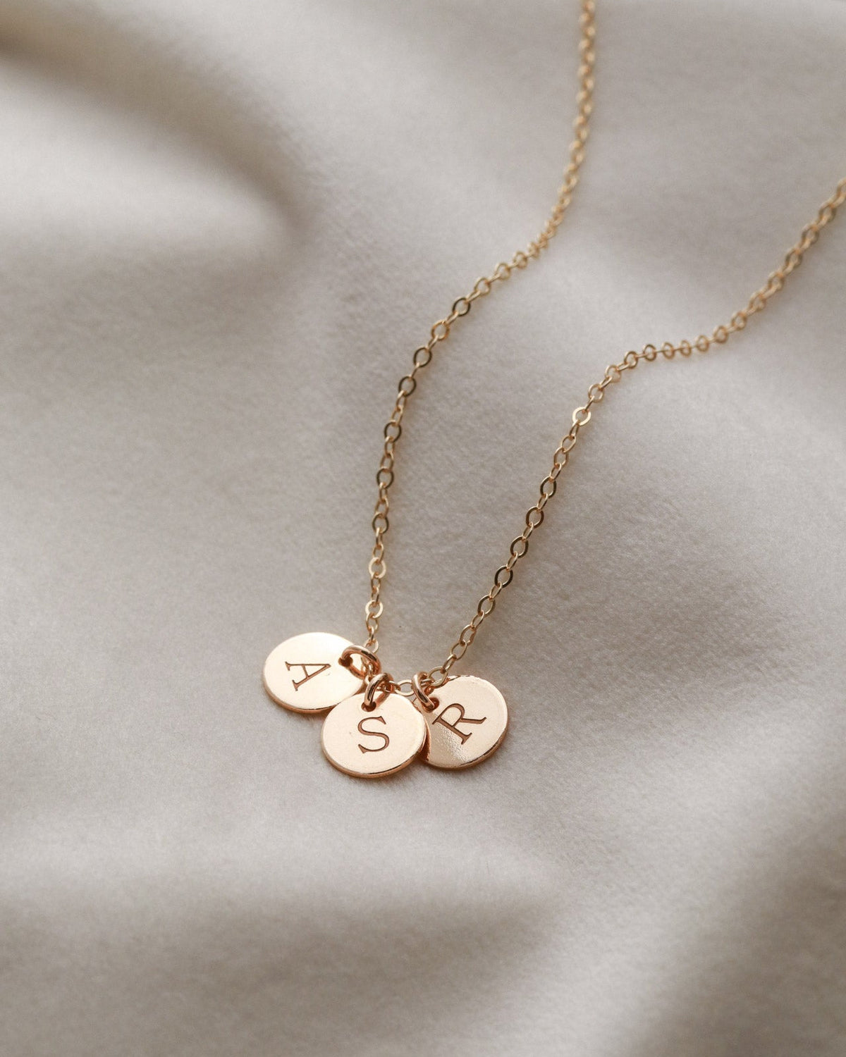 Rose gold necklace with three round pendants on a beige fabric background