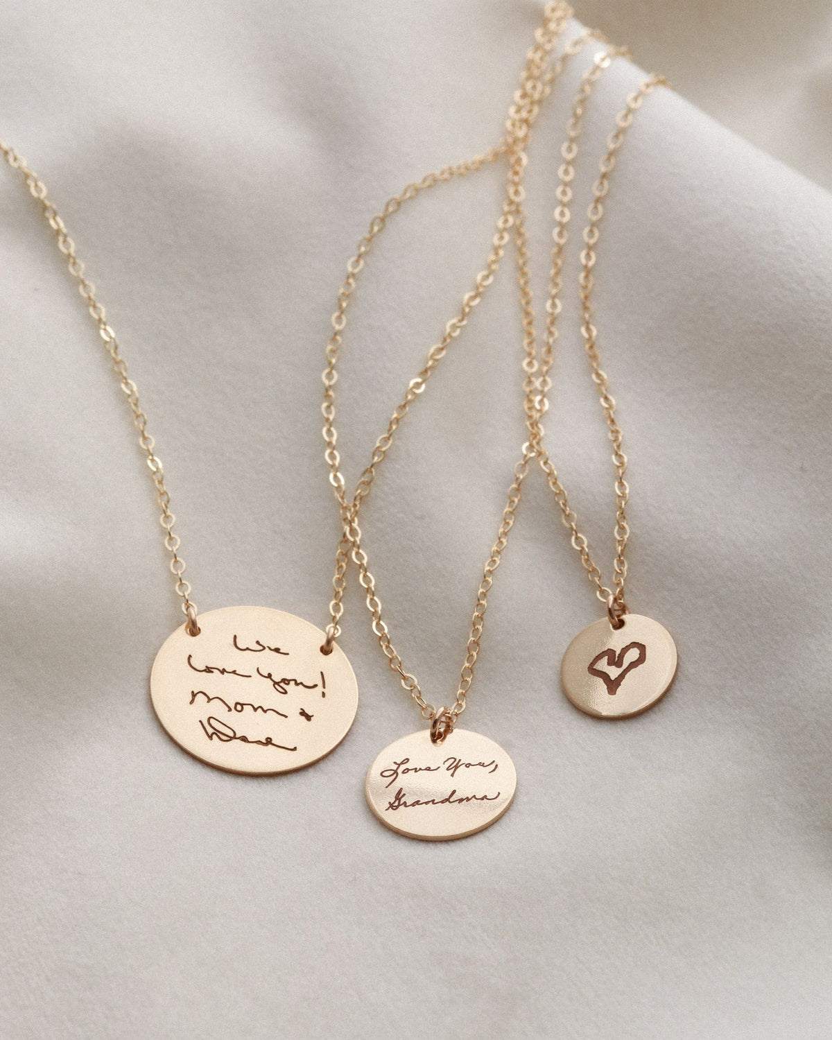 Three gold necklaces with engraved pendants on a light gray background
