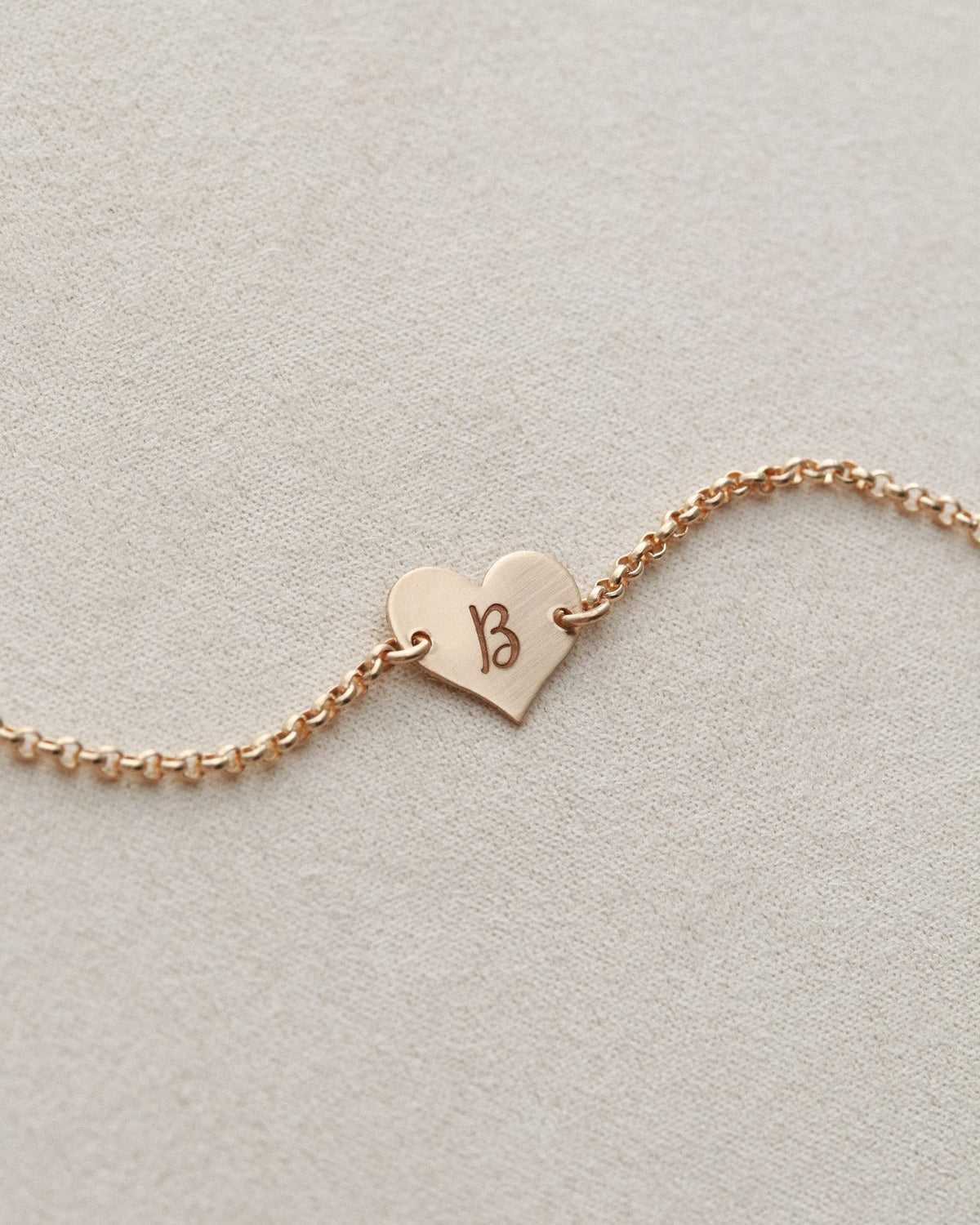 Rose gold bracelet with a heart-shaped tag on a light gray background