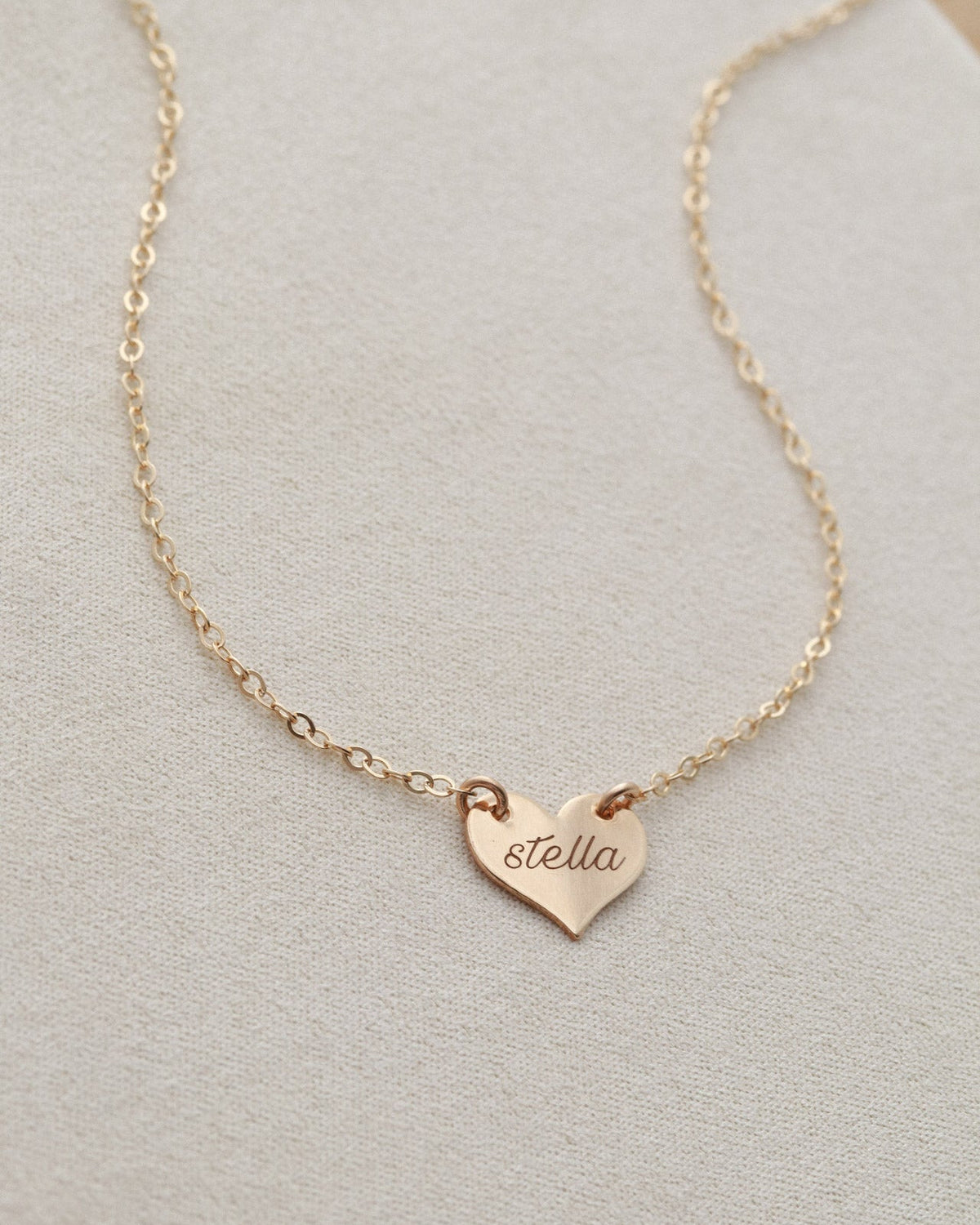 Gold necklace with a heart-shaped pendant on a light gray background