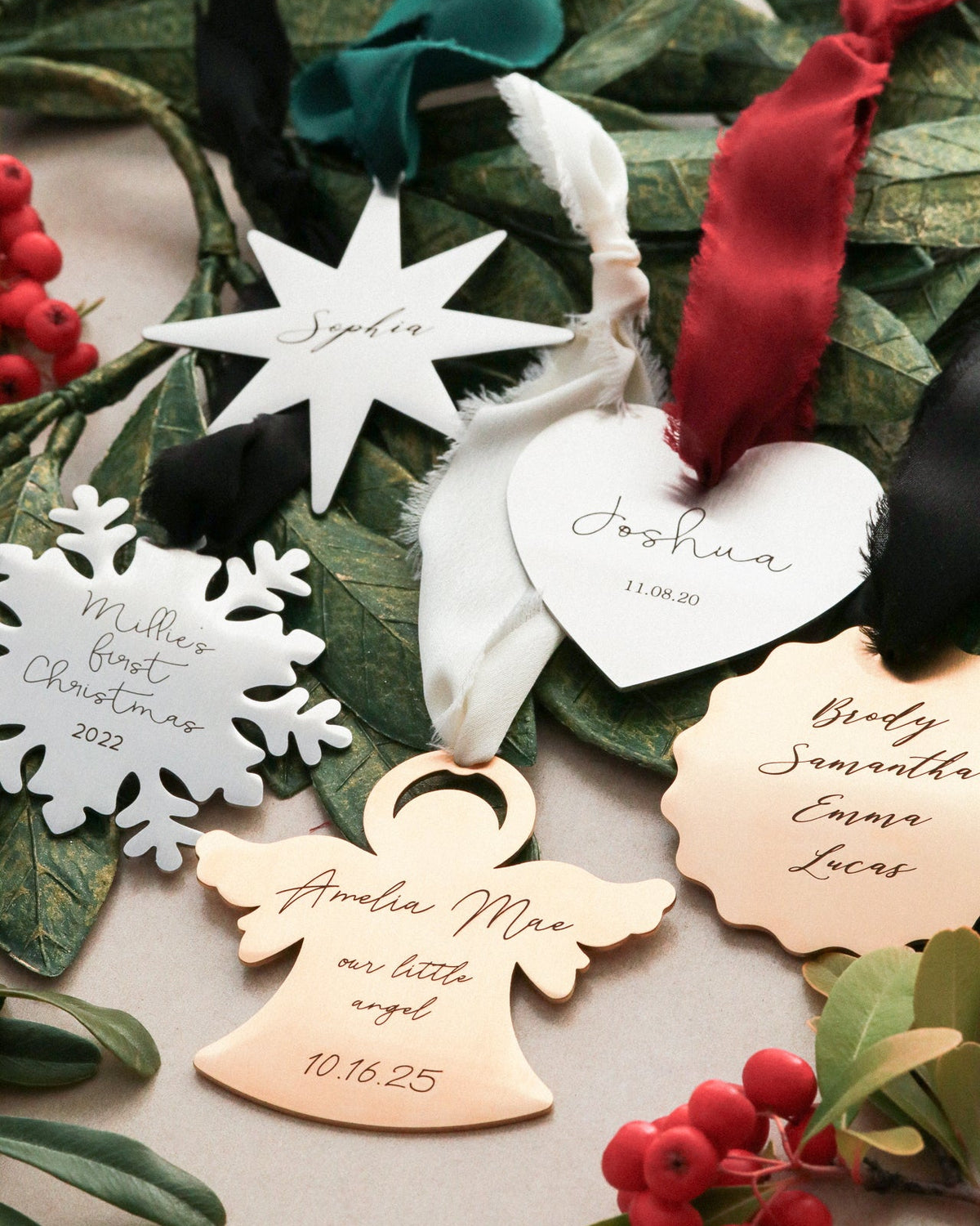 Personalized Christmas ornaments with names on a decorative background with greenery and berries.