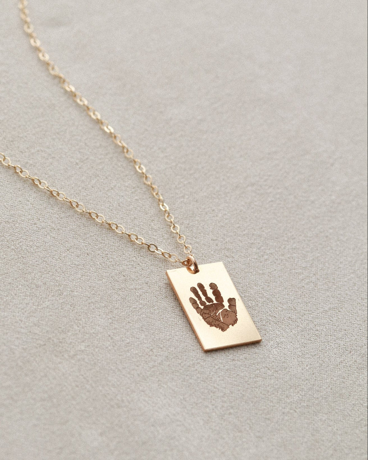 Gold necklace with a hand-shaped pendant on a light gray background