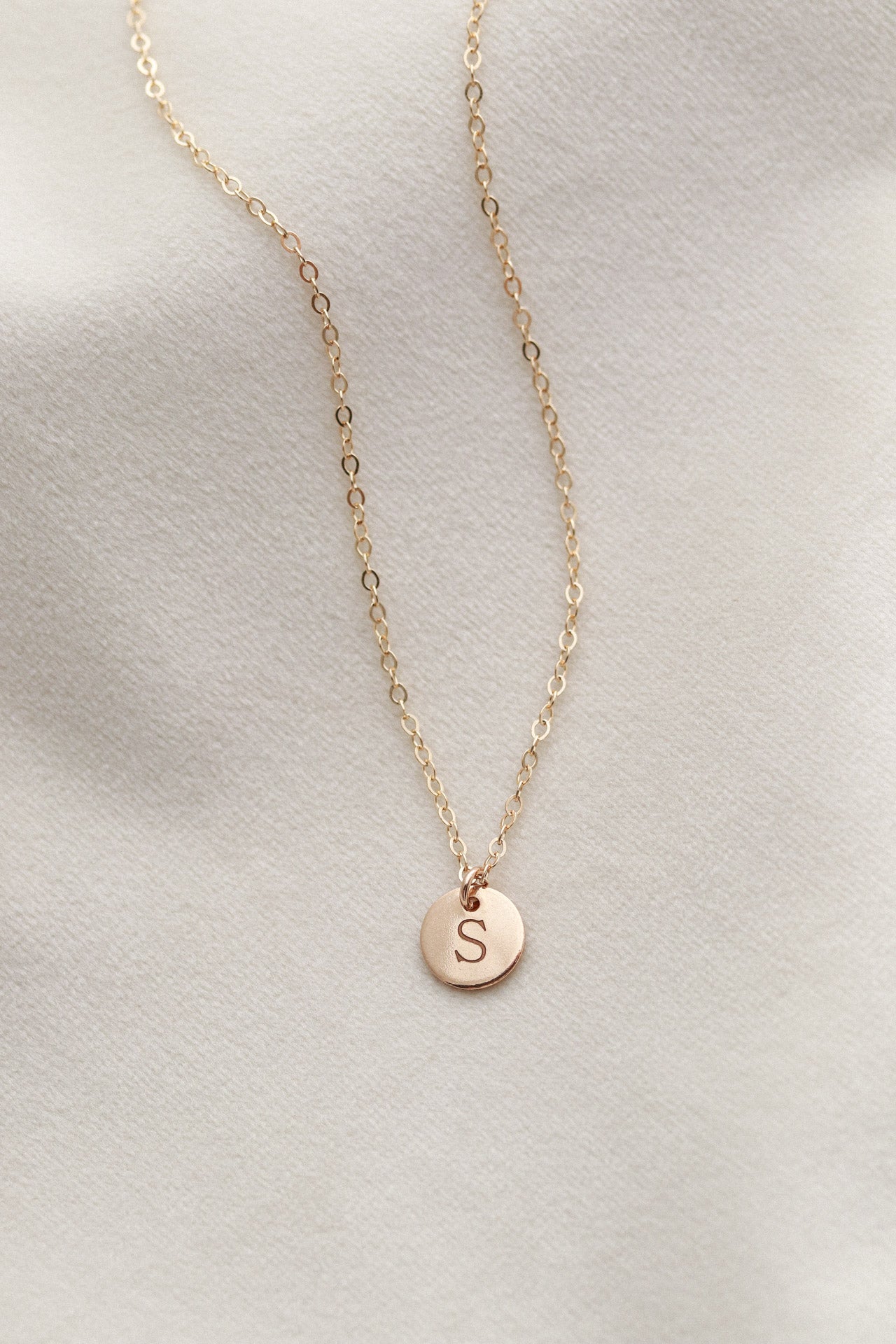 Gold necklace with a round pendant featuring the letter 'S' on a light gray background