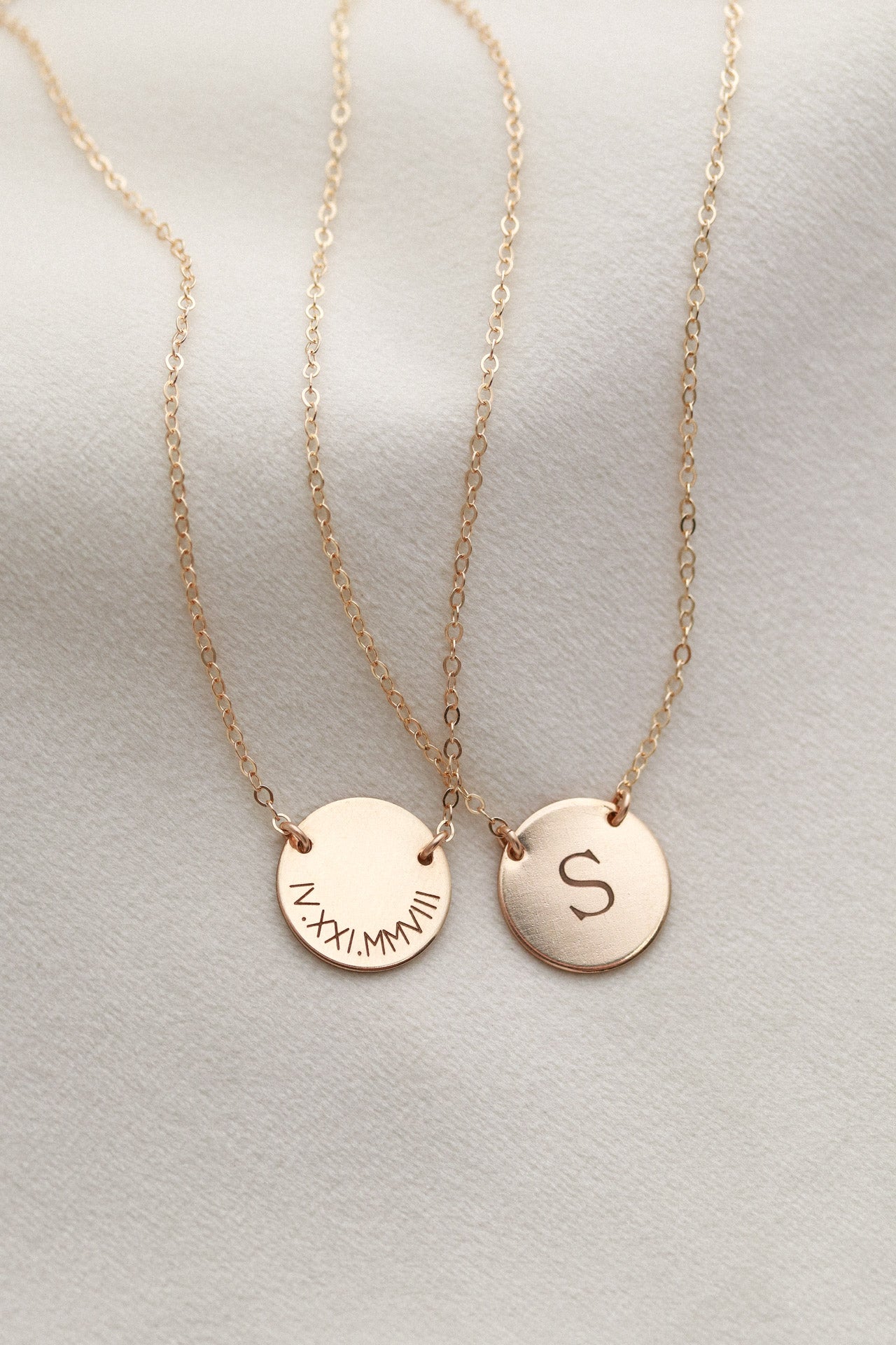 Two gold necklaces with engraved letters on a light gray background
