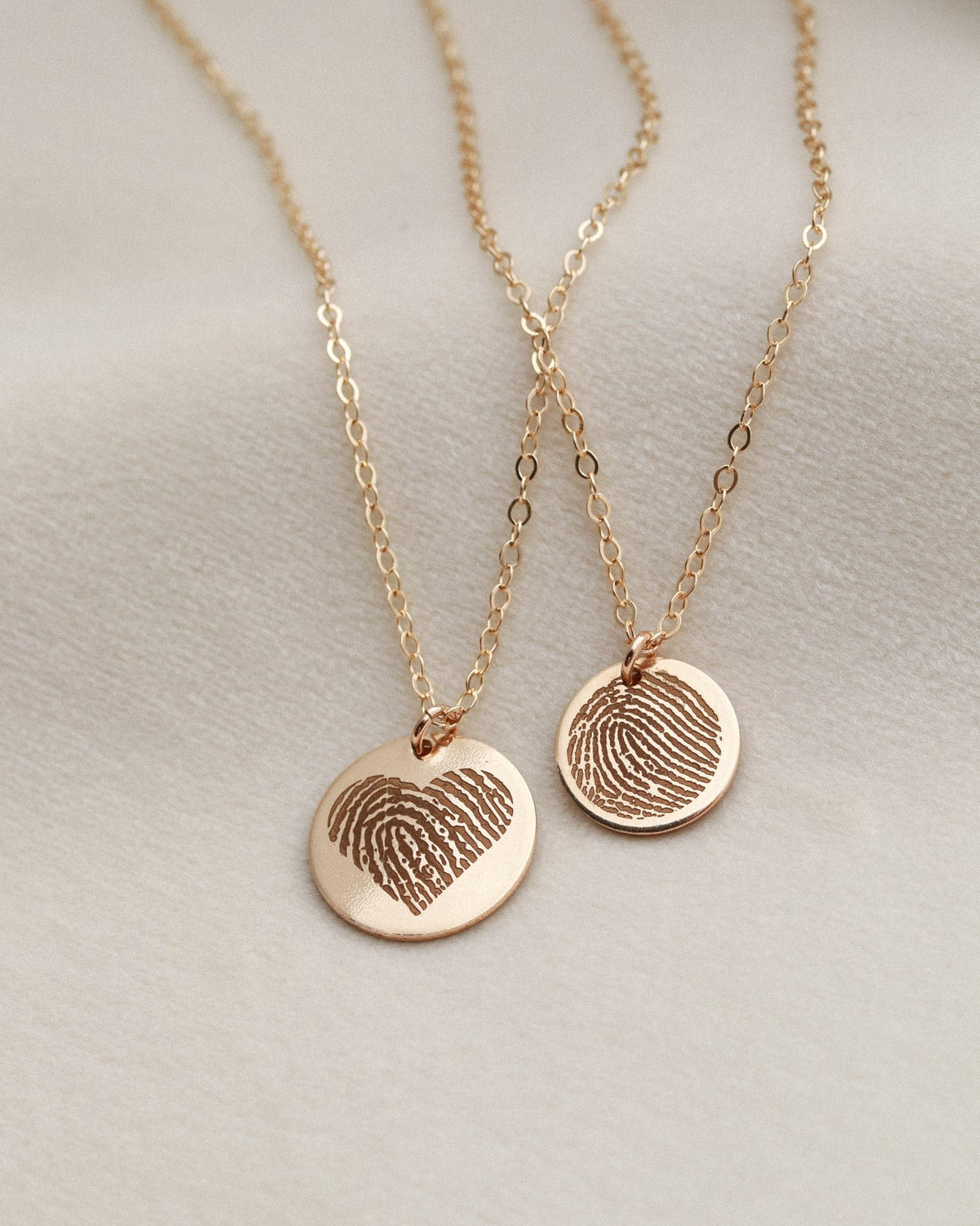 Two gold necklaces with fingerprint pendants on a light gray background