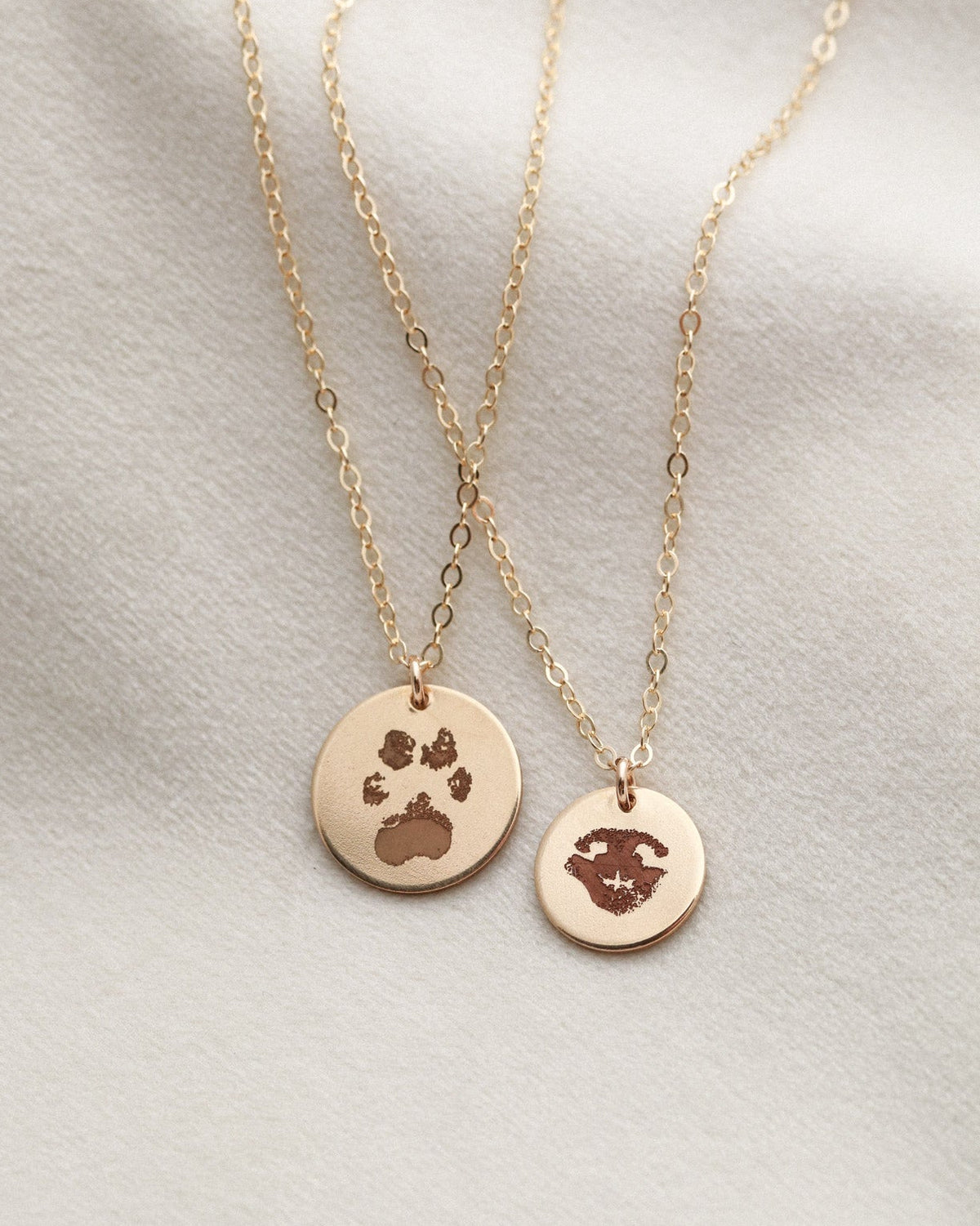 Two gold necklaces with paw print pendants on a light gray background