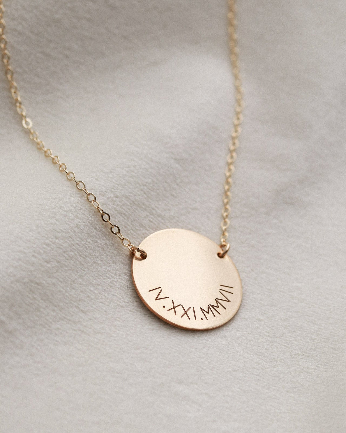 Rose gold necklace with engraved pendant on a light gray background
