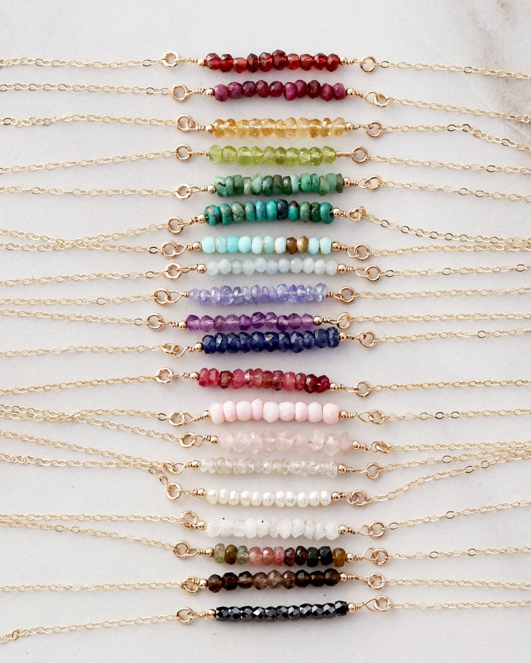 A collection of gemstone bar necklaces with various colored gemstones, laid out in a row on a light background.