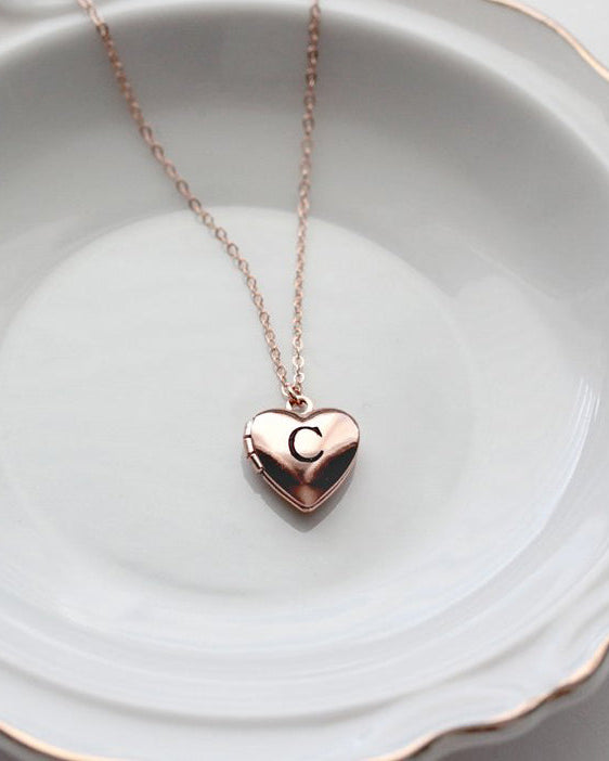 A gold-filled heart-shaped children's locket necklace with the letter 'C' engraved on it, displayed on a white plate.
