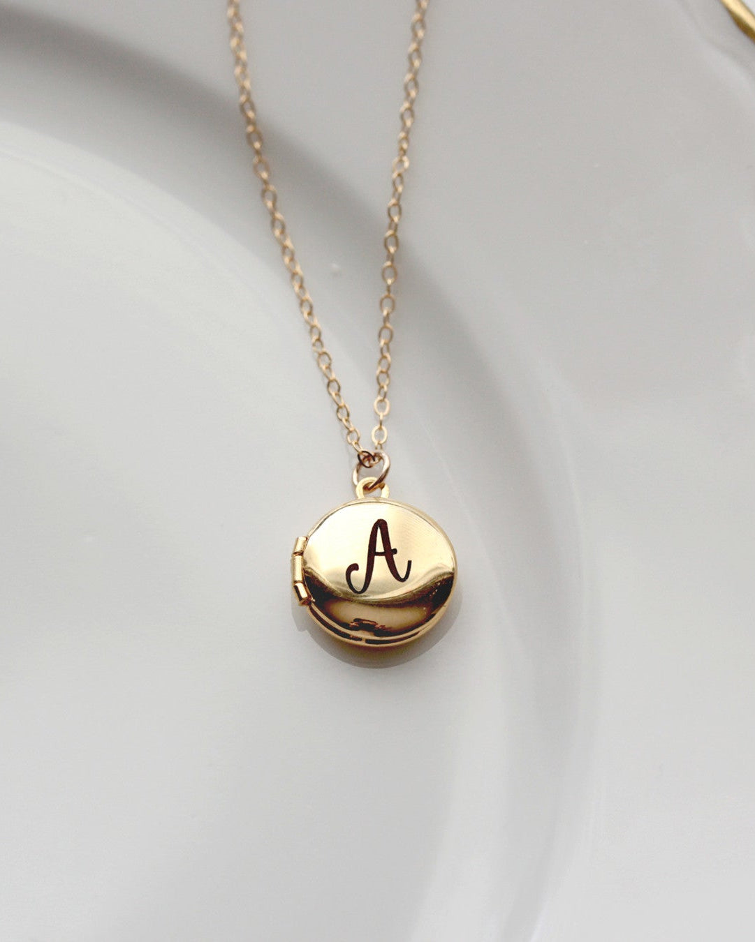 A gold-filled locket necklace with a single letter 'A' engraved on the front, displayed on a white plate.