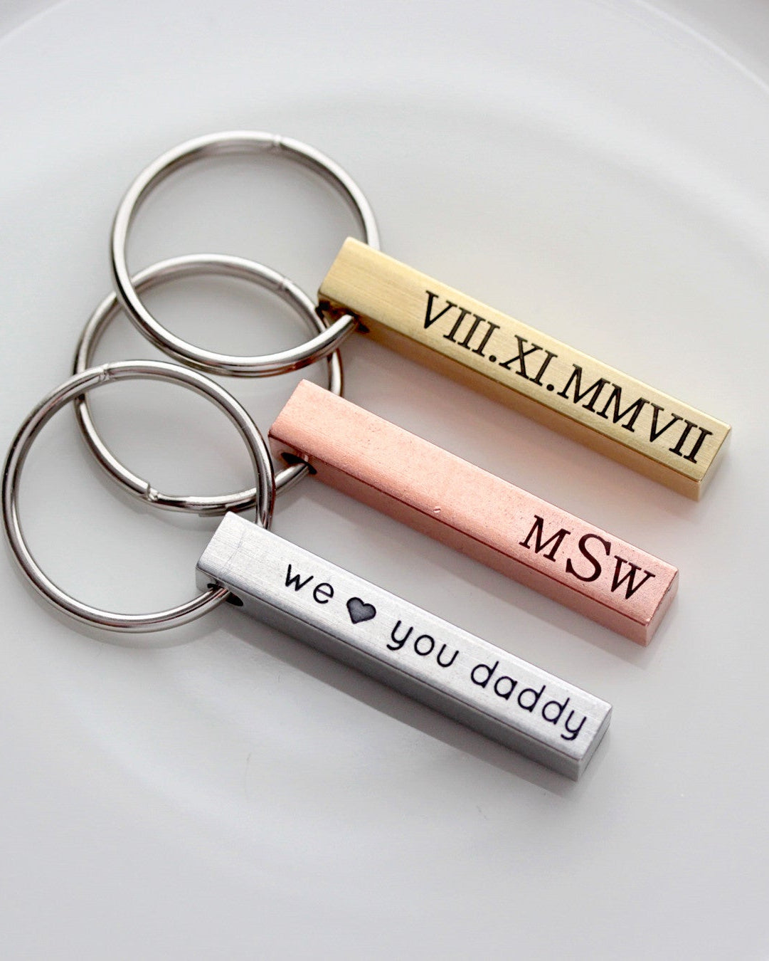 A selection of engraved keychains made from silver, brass, and copper materials, displayed on a white plate.