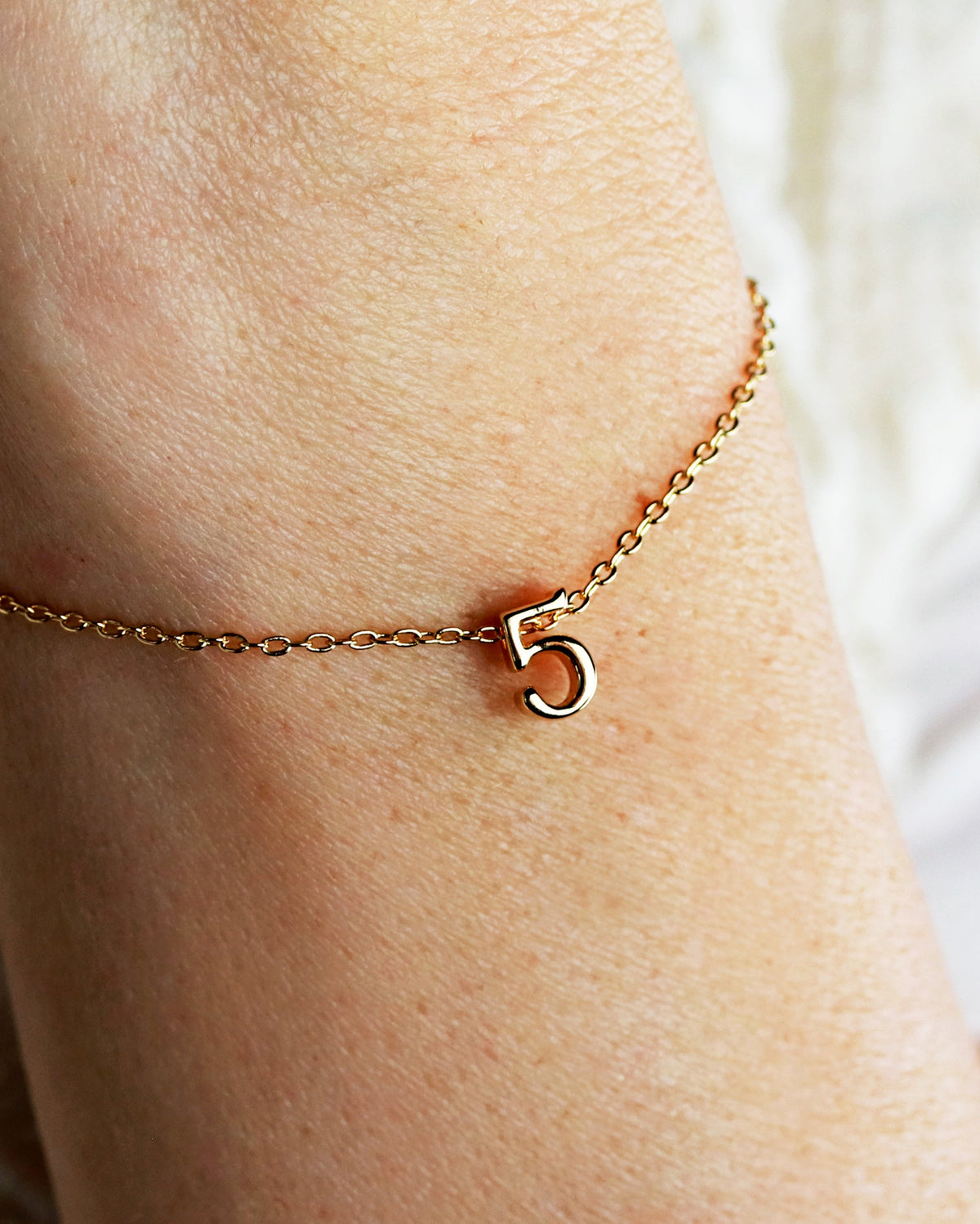 A gold-plated bracelet with a single number charm on a person's wrist.
