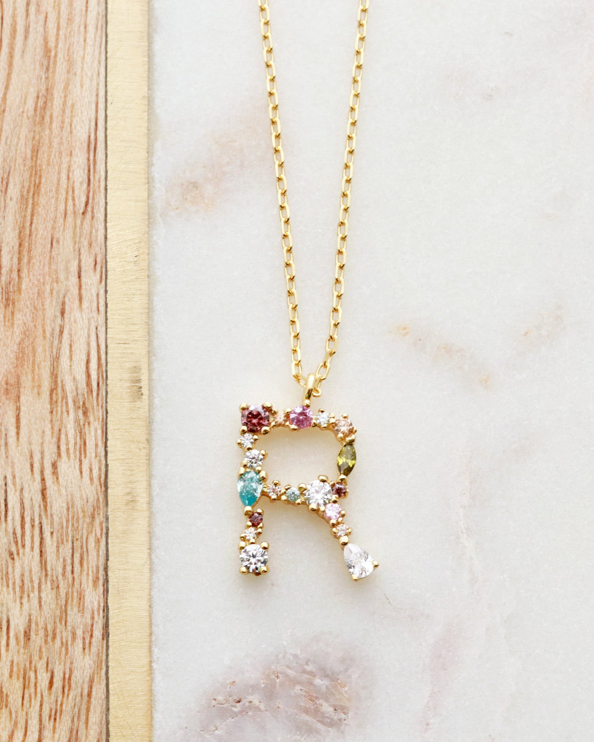 A gold-plated sterling silver necklace with a crystal initial pendant on a chain laid out on a marble surface.