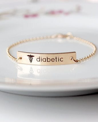 A gold-filled medical alert bracelet with the word 'diabetic' and a symbol engraved on it, displayed on a white plate.