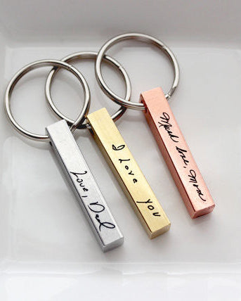 Three keychains with bars engraved with handwriting in silver, brass, and copper colors, displayed in a white dish.