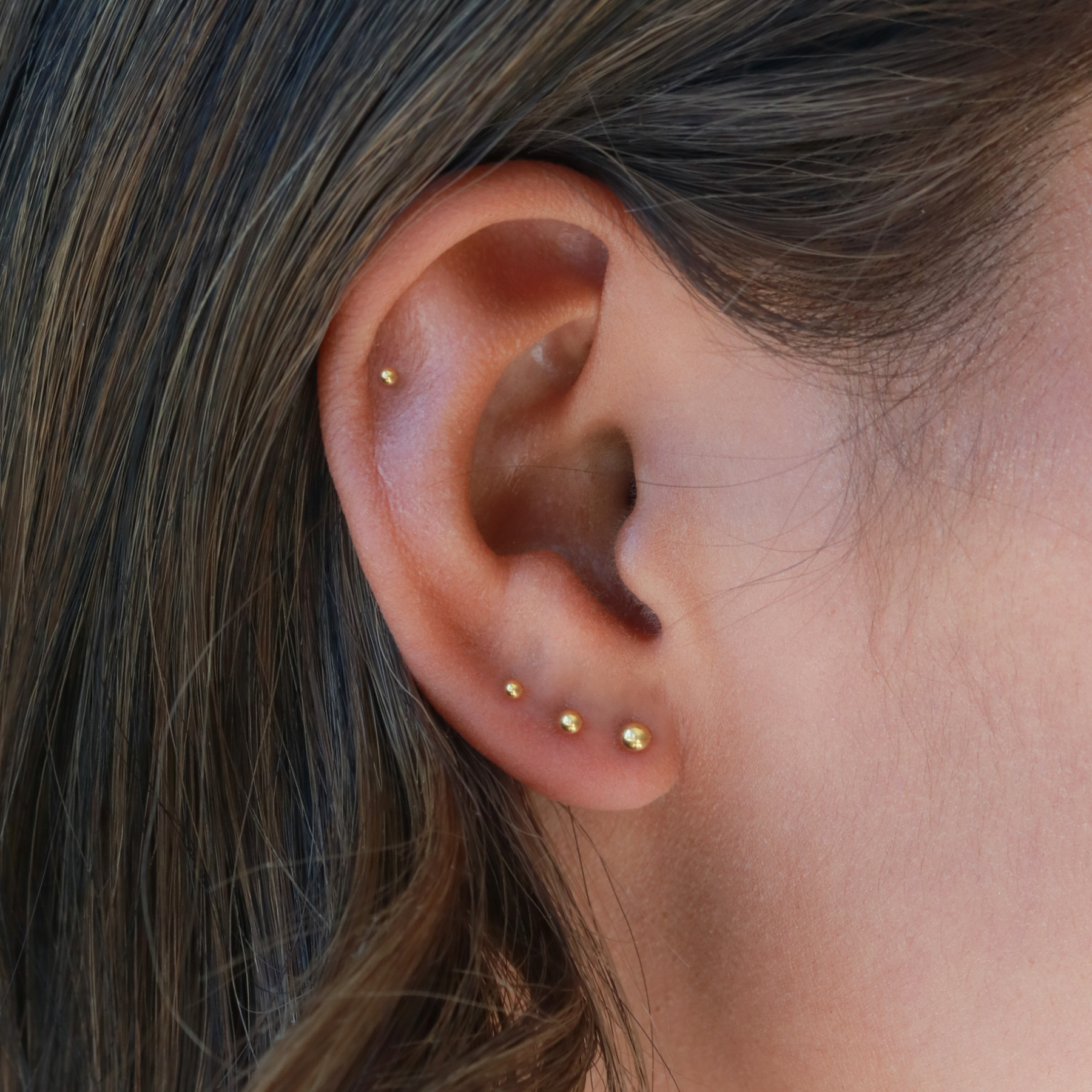 A close-up view of a person's ear adorned with multiple gold earrings.
