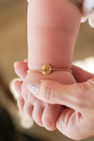 A person's hand holding a baby's wrist, with a bracelet featuring a letter on it.