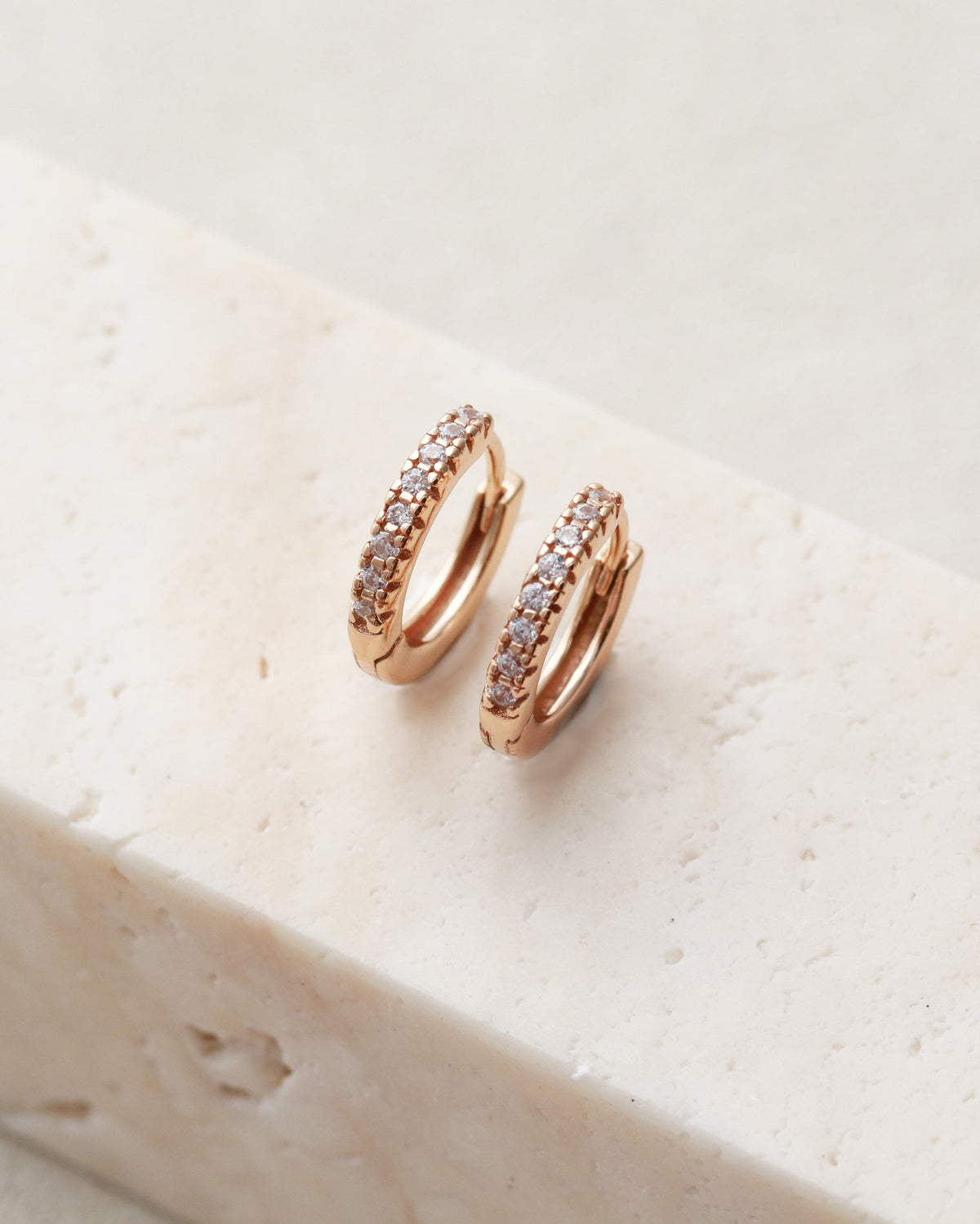 Gold hoop earrings with embedded stones on a light stone surface