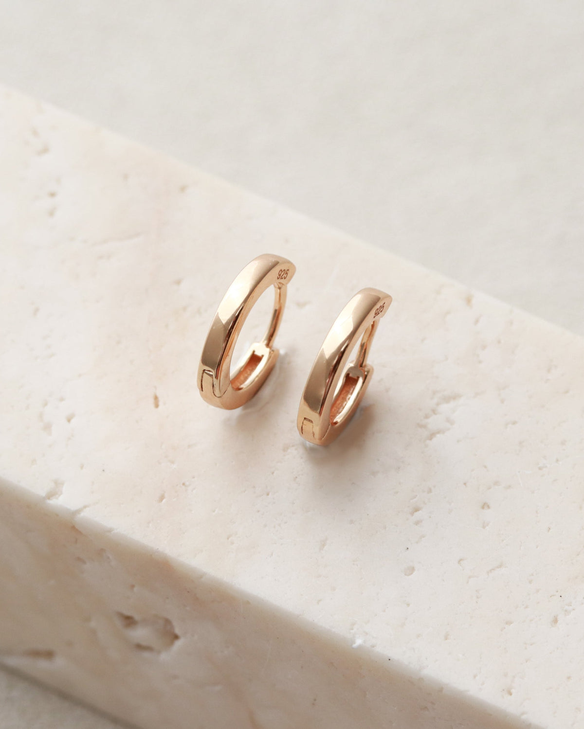 Rose gold hoop earrings on a light stone surface