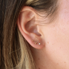 A close-up view of a person's ear with three small gold earrings on the earlobe.