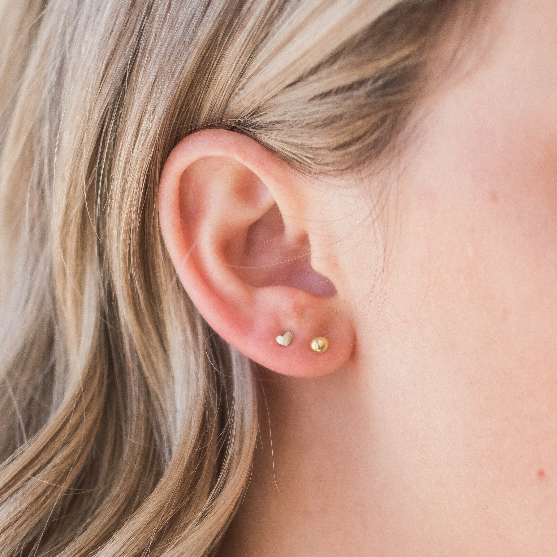 A close-up view of a person's ear with two small gold earrings, one in each ear.