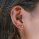A close-up view of a person's ear adorned with multiple earrings, including three small gold earrings and one larger gold earring.