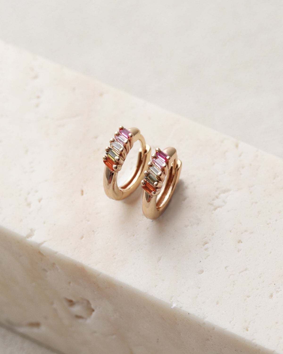 Rose gold hoop earrings with gemstones on a white stone surface