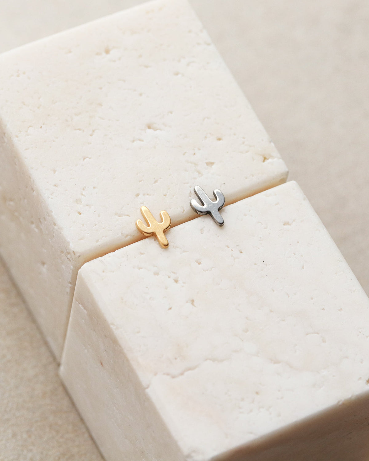 Two small cactus-shaped earrings are placed on a white marble surface.