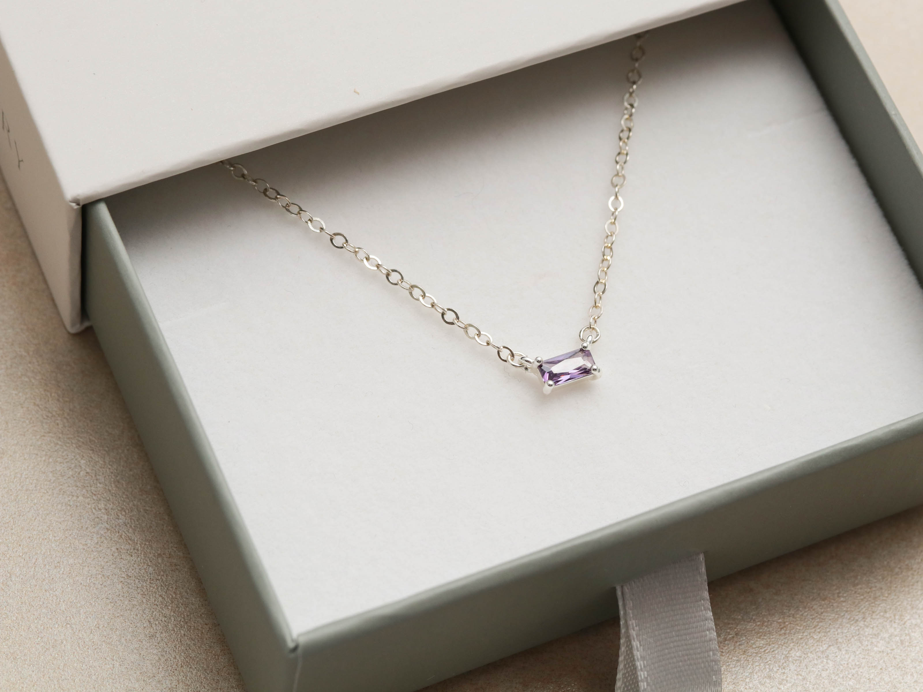 A small custom amethyst birthstone baguette necklace in a gift box.