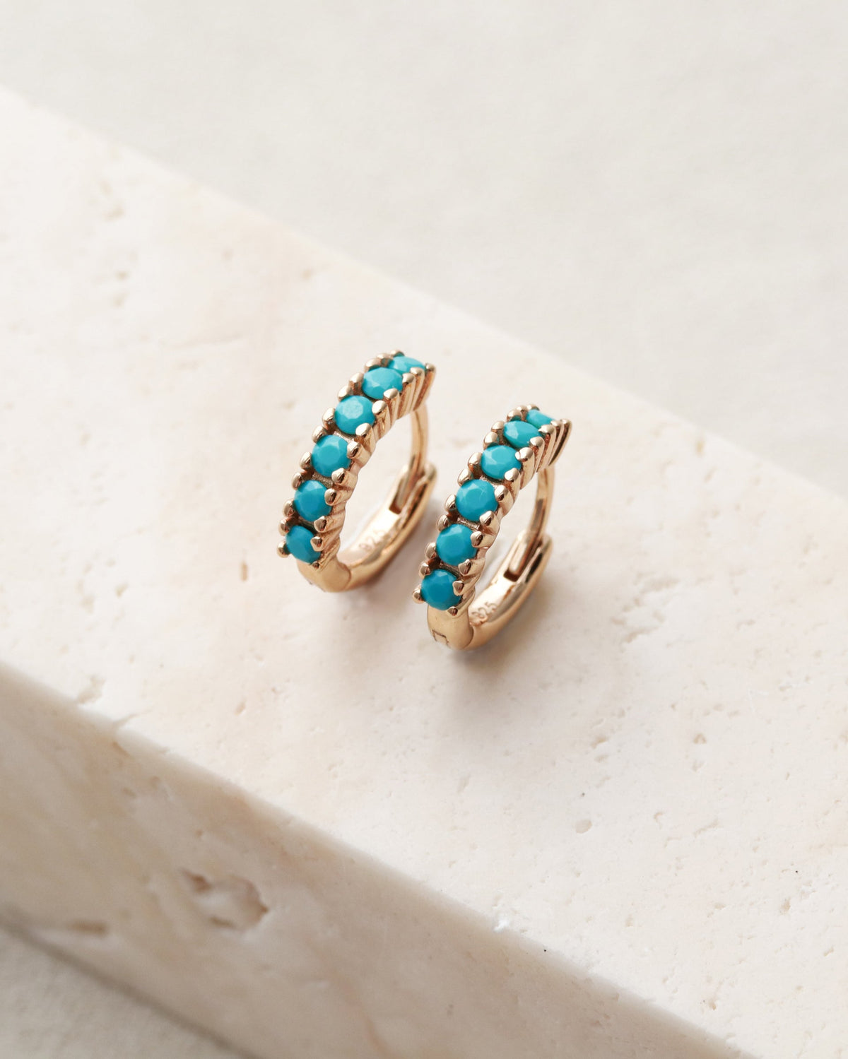 Turquoise hoop earrings on a white stone surface