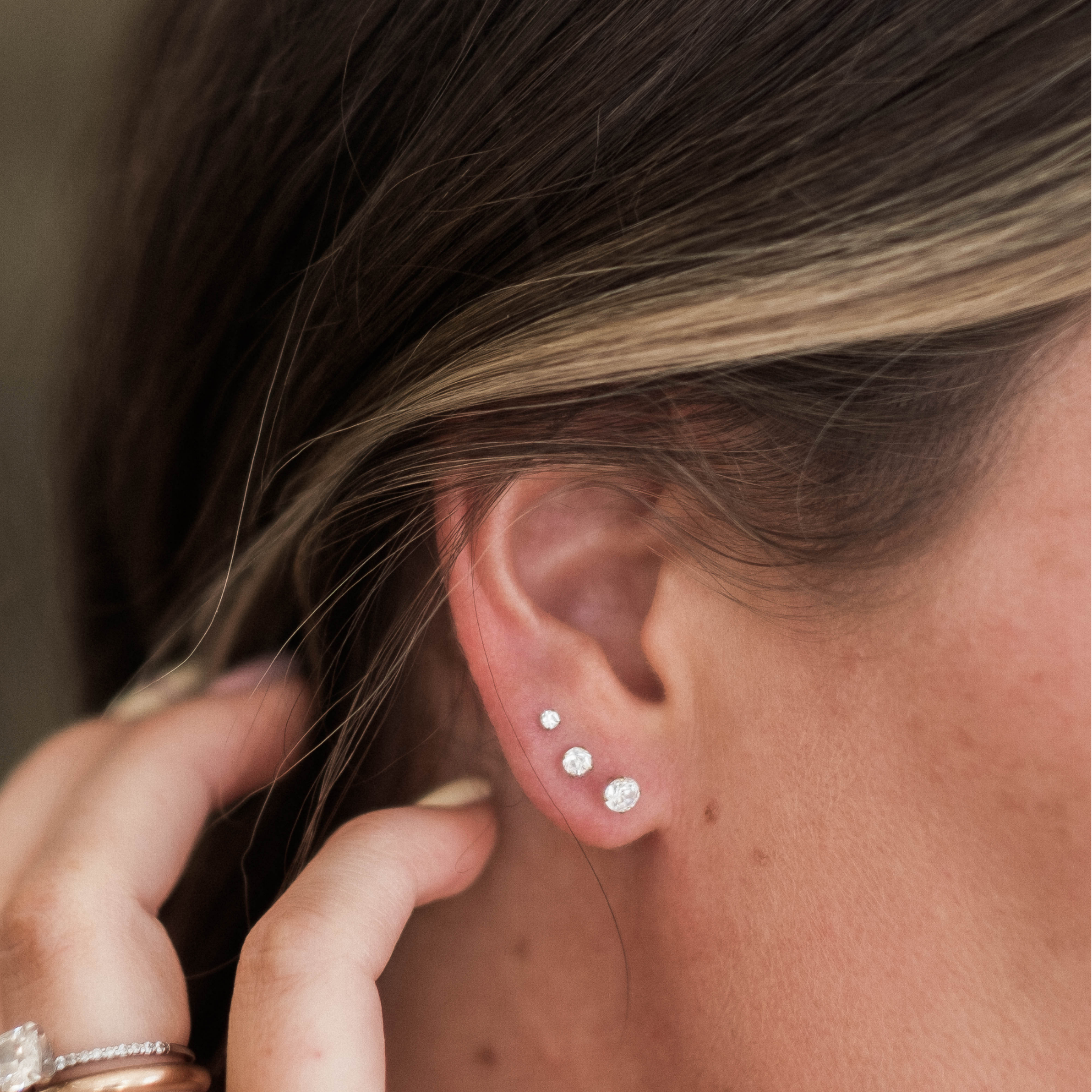 A close-up view of a person's ear adorned with three small, round, white earrings.