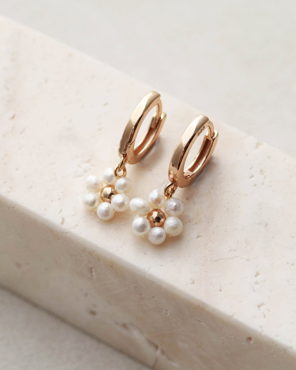 Gold hoop earrings with pearl drops on a white stone surface