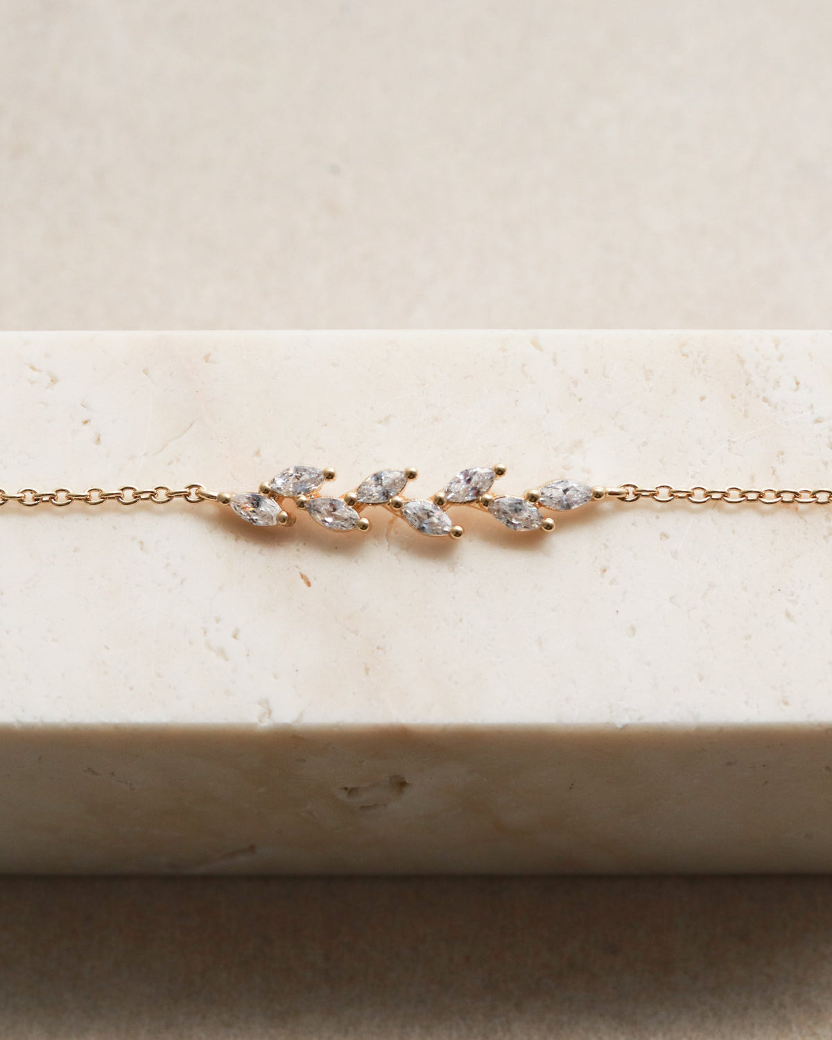 Gold bracelet with diamond accents on a white pedestal.