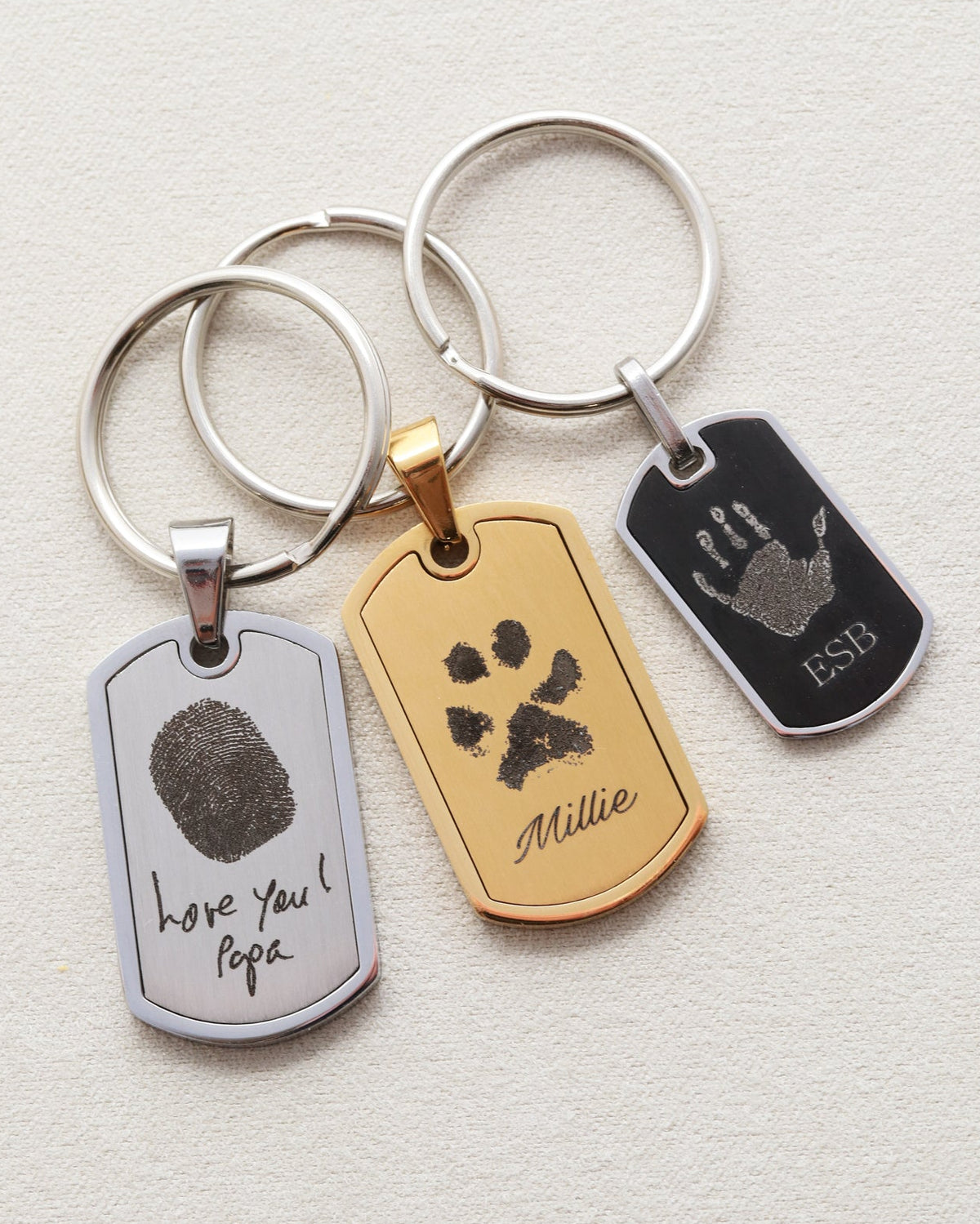 Four keychains with engraved text and paw prints on a light gray background