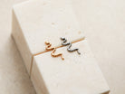 Two small metal snake-shaped earrings are placed on a white surface.