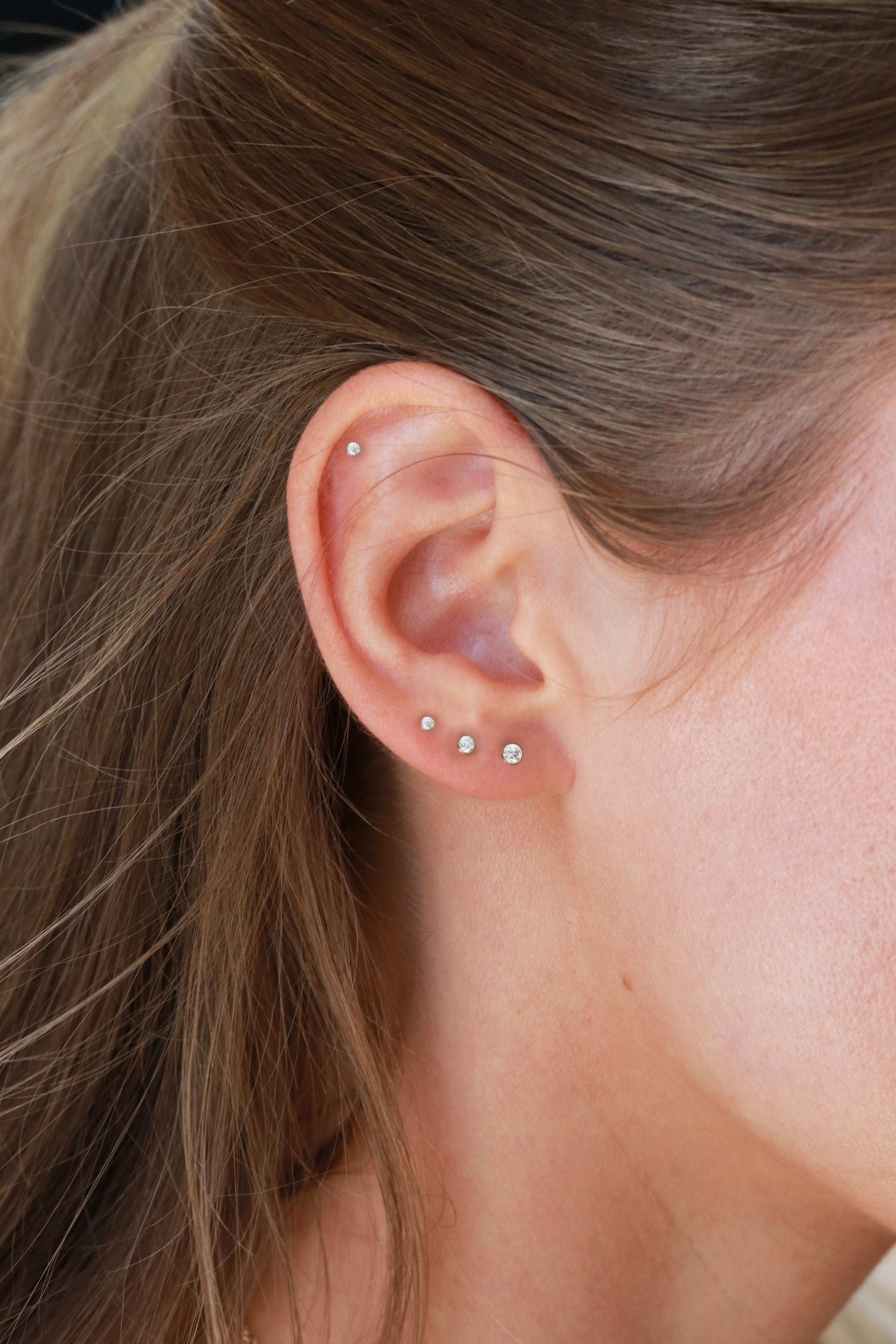 a close-up view of a person's ear adorned with multiple small earrings.